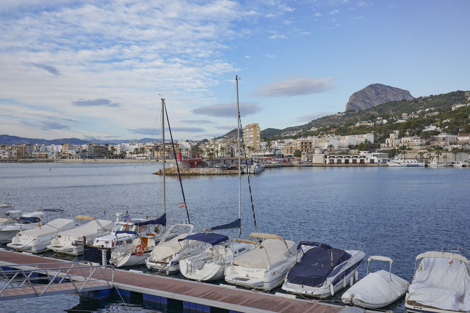 Panoramablick auf den Yachthafen von Jávea mit vertäuten Booten und dem markanten Massiv des Montgó im Hintergrund bei Tageslicht.