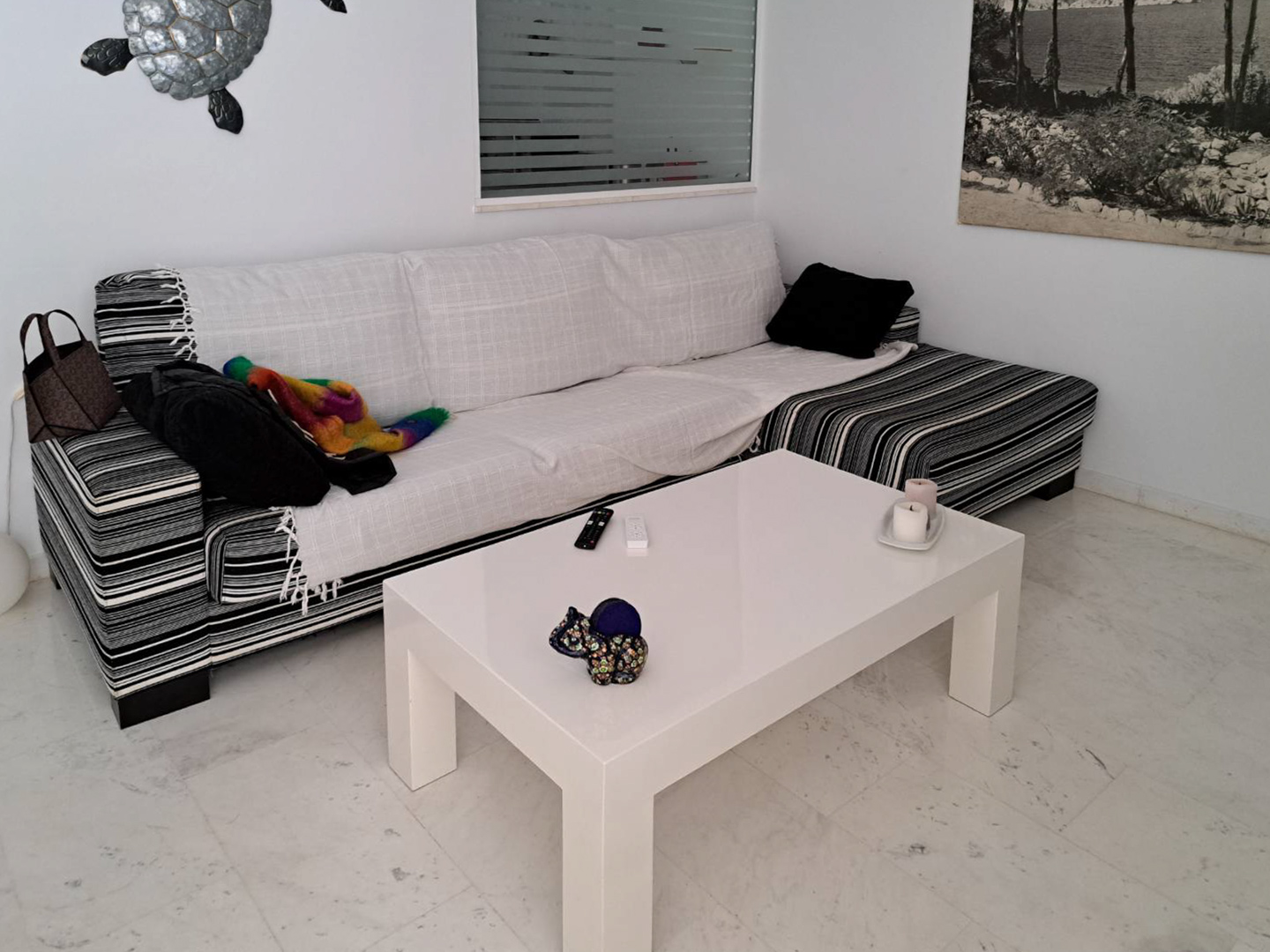 Wohnbereich mit Marmorboden, gestreiftem Ecksofa und einem minimalistischen weißen Couchtisch in hellem, zeitlosem Design.