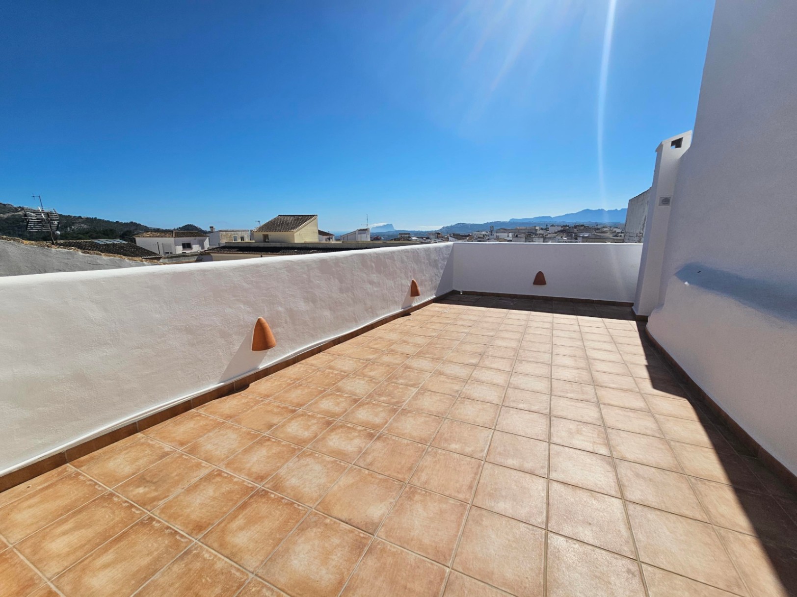 Dachterrasse mit Terrakotta-Fliesen, weiß getünchten Mauern und Panoramablick über das Dorf bis hin zum Meer und dem Peñón de Ifach.