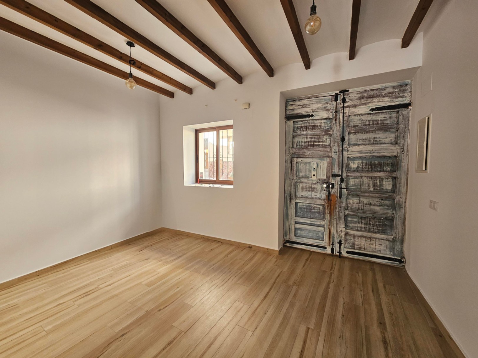 Eingangsbereich mit sichtbaren Deckenbalken aus Holz, hellem Boden in Holzoptik und einer großen, restaurierten rustikalen Doppeltür.