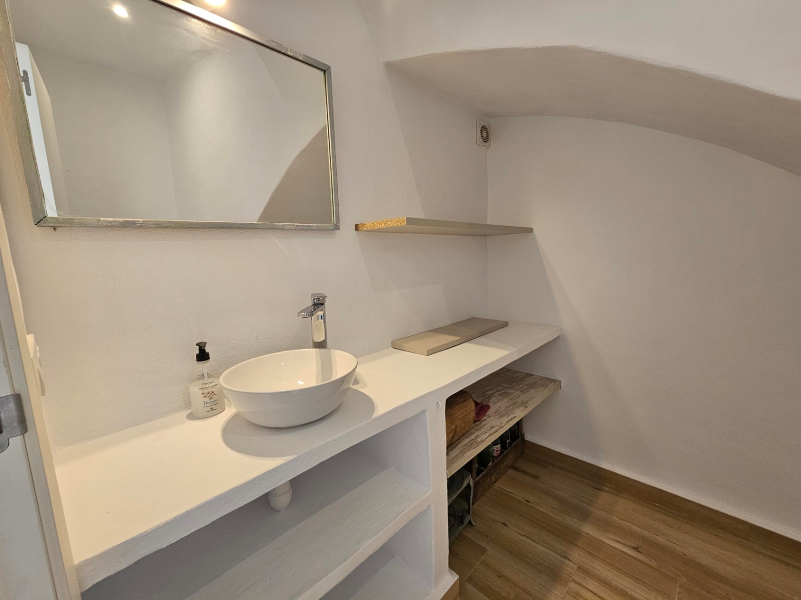 Gäste-WC mit Aufsatzwaschbecken auf gemauerter Konsole, integrierten Regalen, Bodenfliesen in Holzoptik und einer charakteristischen Dachschräge.