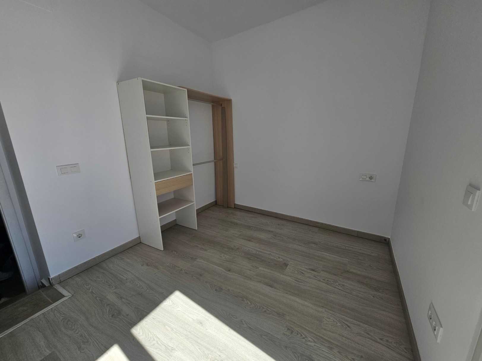 Heller Raum mit hellem Laminatboden, weißen Wänden und einem funktionalen offenen Schranksystem mit Regalen und Kleiderstange.