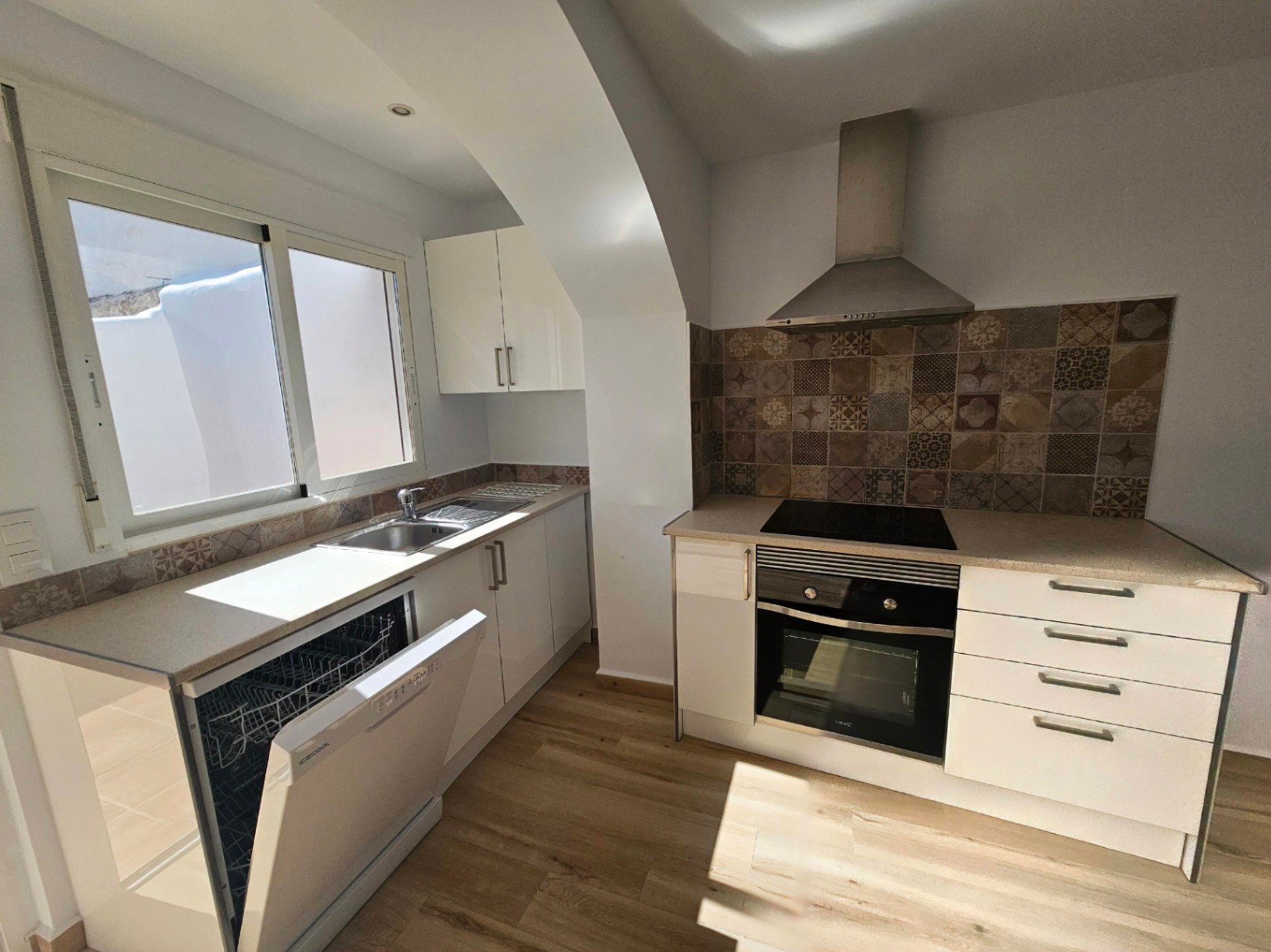 Moderne Küche mit weißen Schränken, Arbeitsplatte in Steinoptik und dekorativem Fliesenspiegel. Ausgestattet mit Einbaugeräten und Blick auf den Innenhof.