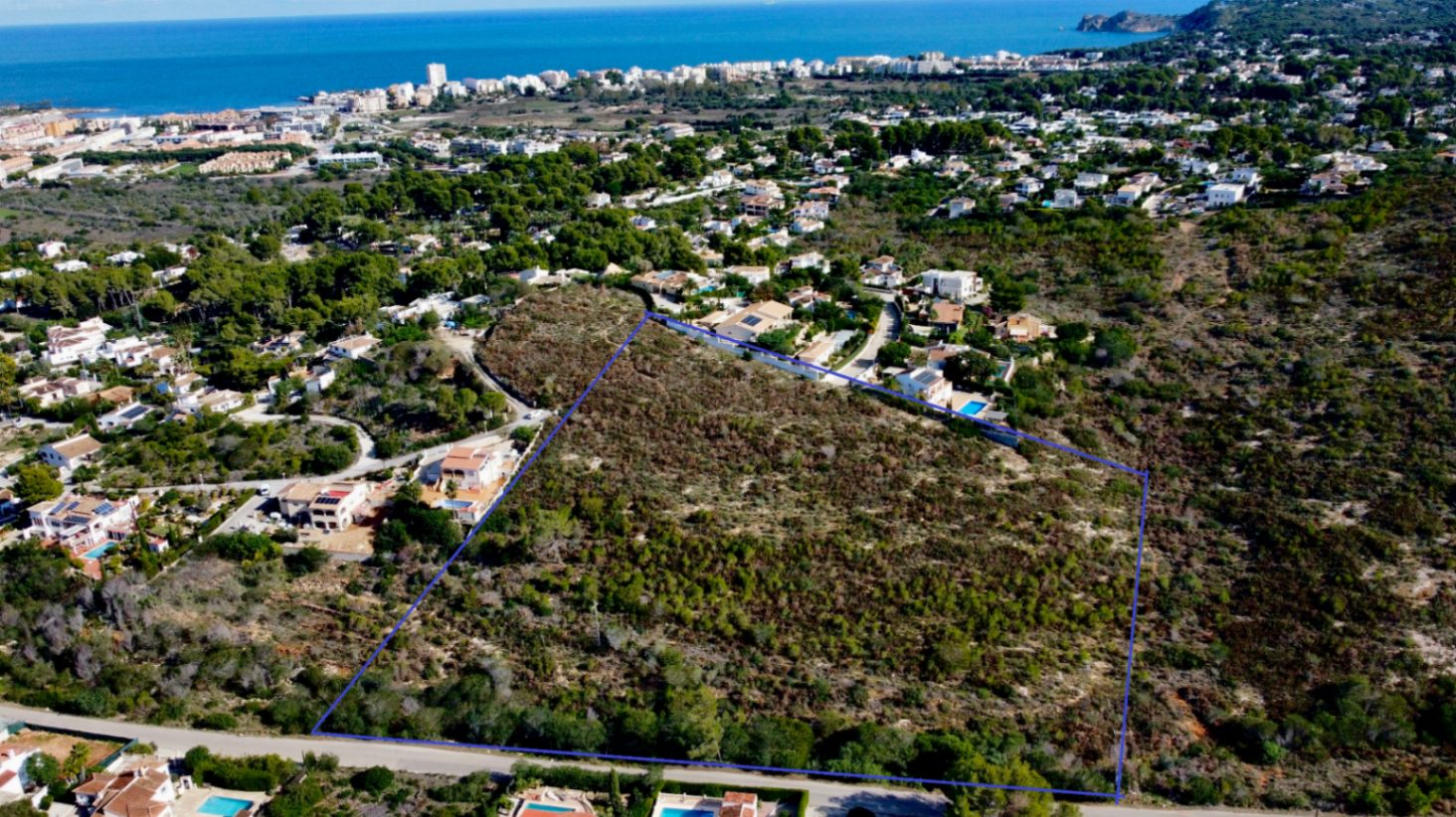 Luftaufnahme des 17.272 m² großen Grundstücks in Jávea, blau umrandet, mit mediterraner Vegetation und Blick auf die nahegelegene Küste und das Meer.