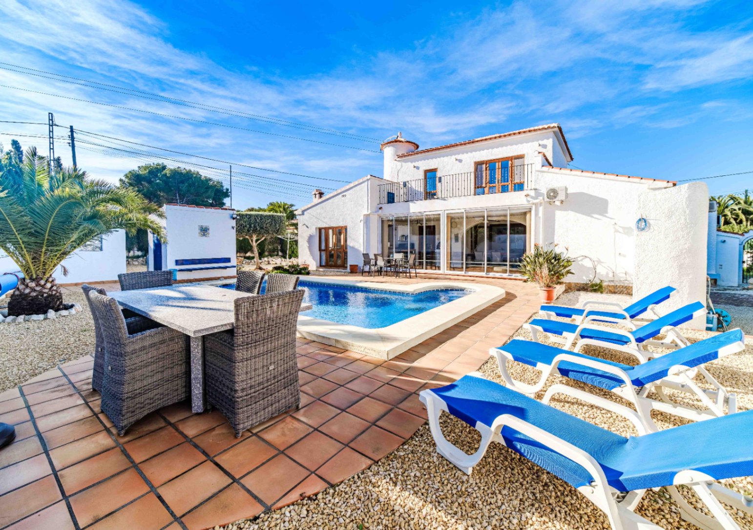 Außenansicht der Villa mit privatem Pool, Essbereich im Freien und Sonnenliegen vor der traditionellen weißen Fassade mit verglaster Terrasse.
