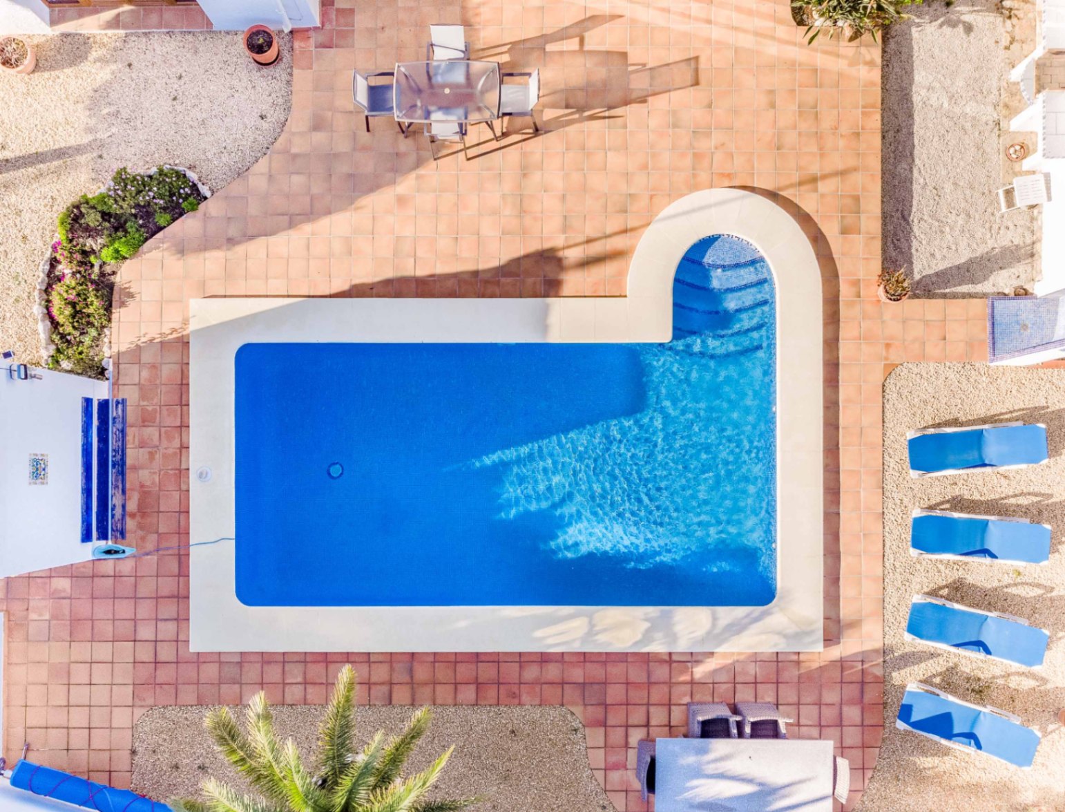 Draufsicht auf den rechteckigen Pool mit römischer Treppe, umgeben von einer Terrakotta-Terrasse, blauen Sonnenliegen und verschiedenen Sitzbereichen im Freien.