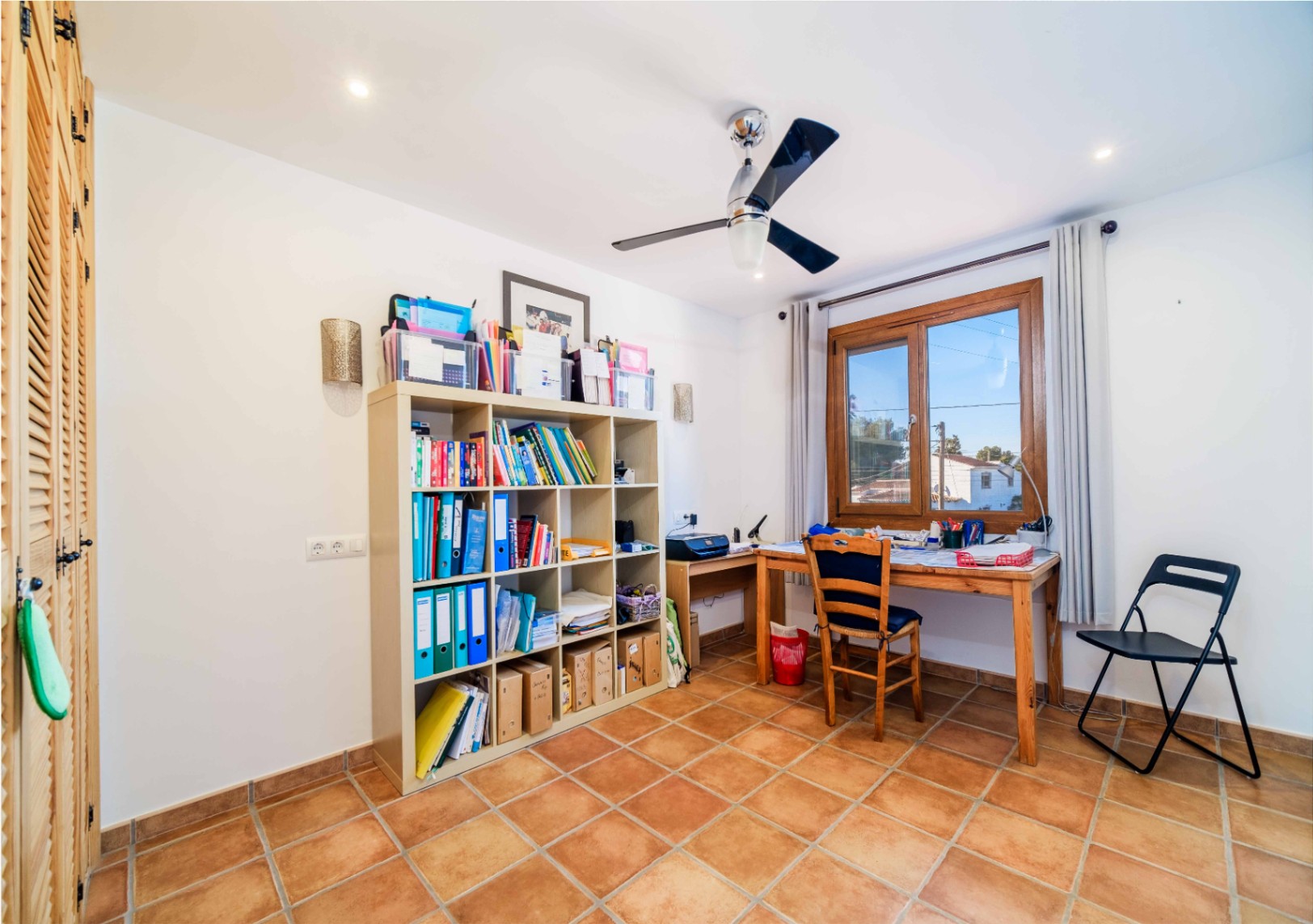 Funktionales Arbeitszimmer mit rustikalen Fliesen, modularem Regal und Holzschreibtisch. Ausgestattet mit Deckenventilator, Einbaustrahlern und Einbauschränken mit Lamellentüren.