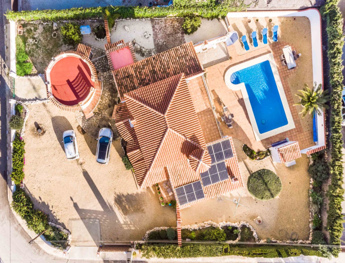 Luftaufnahme der Villa mit Darstellung des L-förmigen Pools, der Photovoltaikanlage auf dem Ziegeldach und des markanten Rundturms auf dem Gelände.