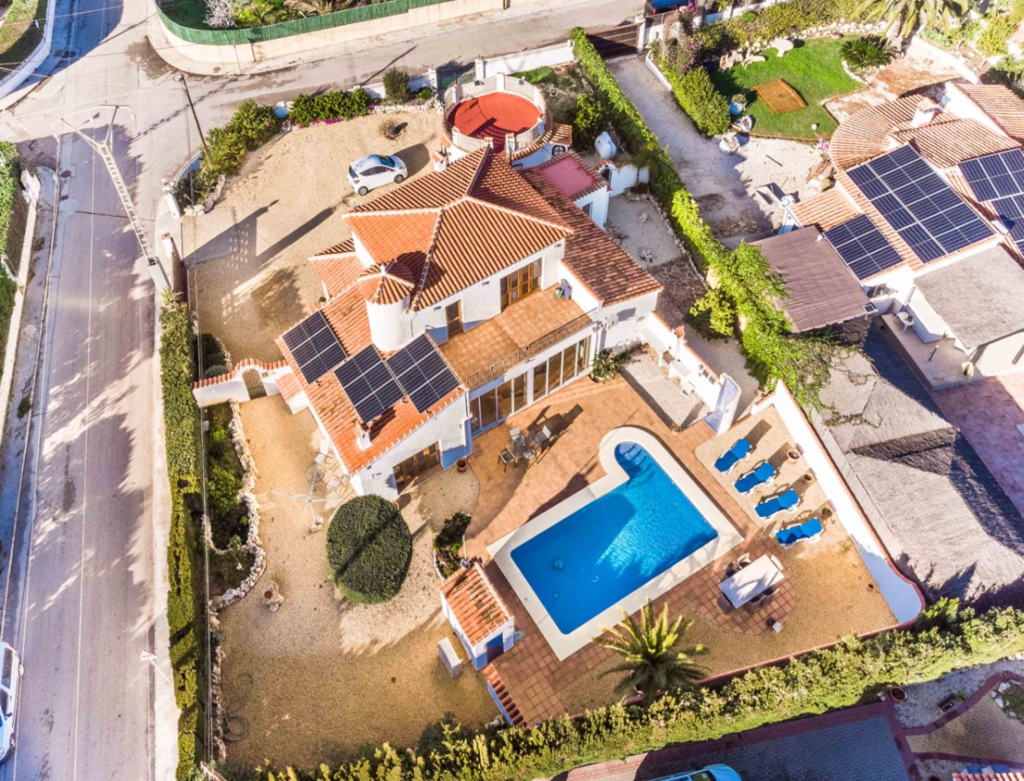 Luftaufnahme der Villa mit privatem Pool, Sonnenterrasse mit Liegen, Photovoltaikanlage auf dem Dach und dem großzügigen Eckgrundstück.