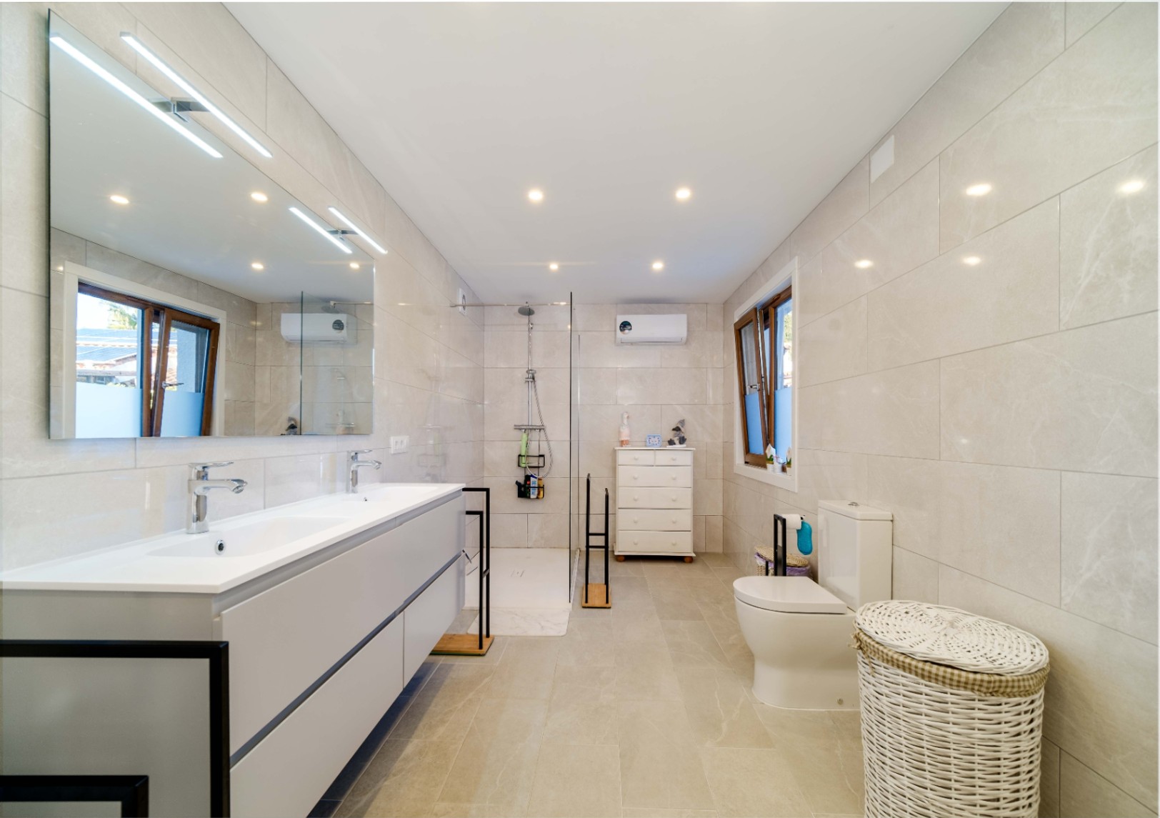 Modernes Badezimmer mit Doppelwaschtisch, grauem Unterschrank und großem Lichtspiegel. Ausgestattet mit begehbarer Dusche, neutralen Fliesen und Deckeneinbaustrahlern.