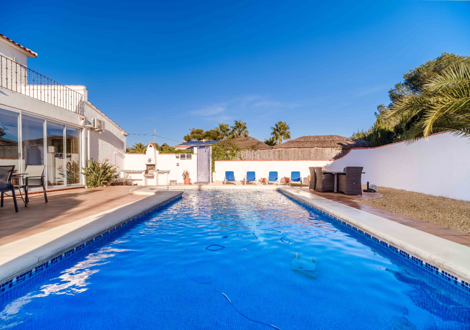 Rechteckiger, blau gefliester Pool mit Terrakotta-Terrasse, integriertem Grillbereich und sichtbaren Sonnenkollektoren auf dem Dach im Hintergrund.