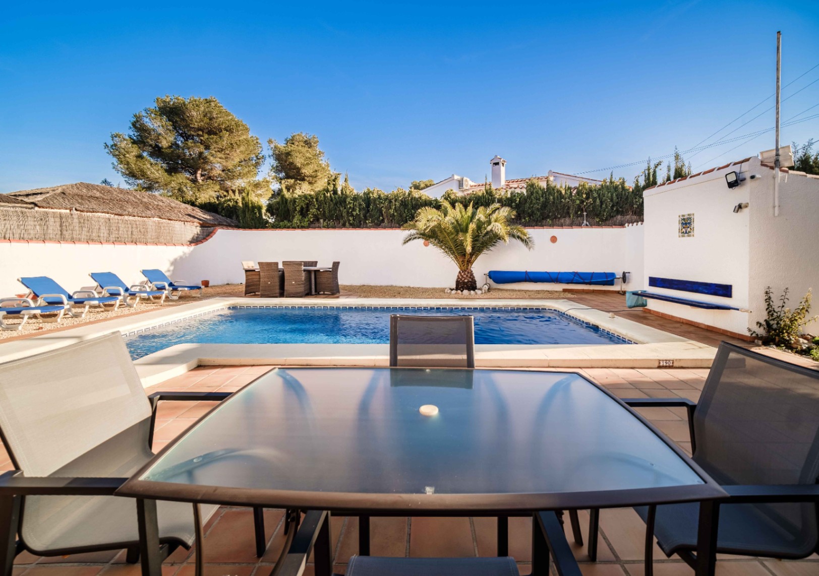 Rechteckiger Swimmingpool mit Terrakotta-Terrasse, Sonnenliegen auf Kies und Essbereich im Freien. Die Anlage ist von weißen Mauern und mediterranen Pflanzen umgeben.