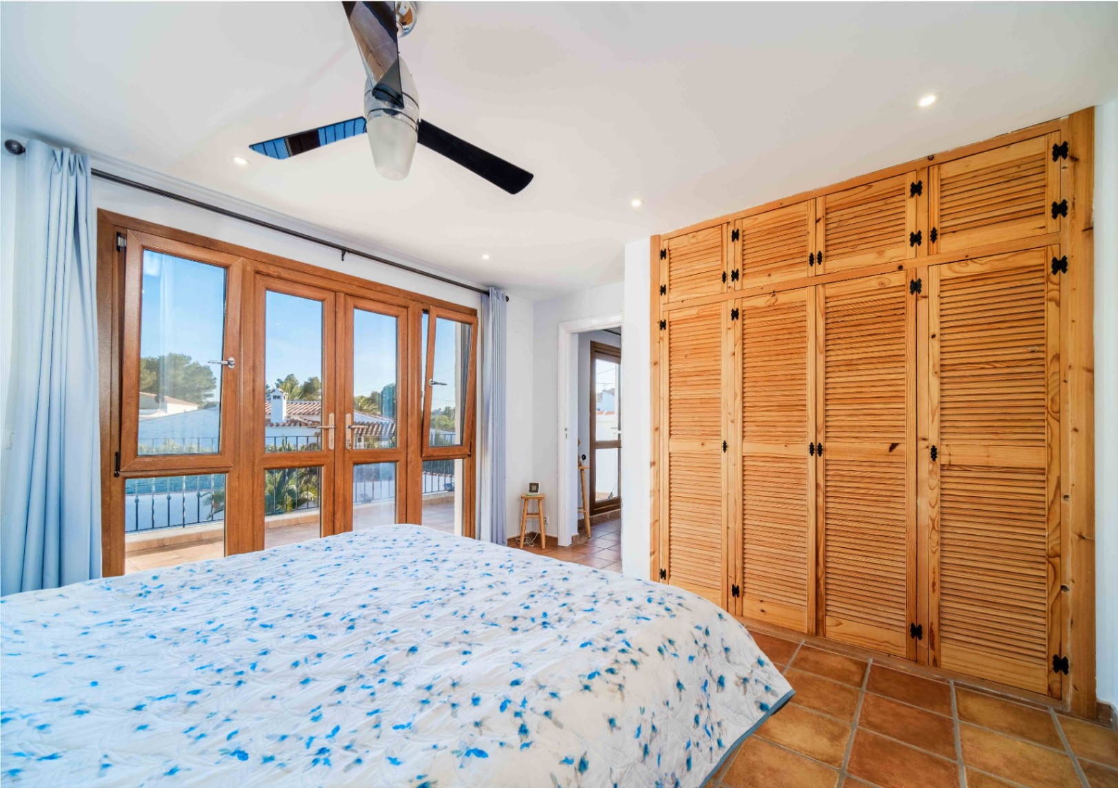 Schlafzimmer mit hölzernen Einbauschränken, Terrakottafliesen und großen Fenstertüren, die direkten Zugang zum Balkon bieten.