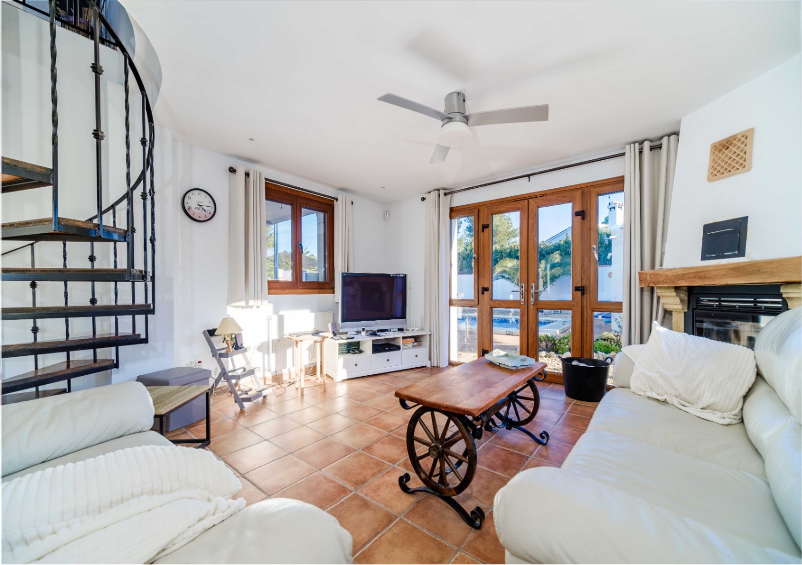Wohnbereich mit Terrakottafliesen, weißen Ledersofas und Wendeltreppe. Große Holzrahmentüren bieten einen direkten Zugang zum Poolbereich.