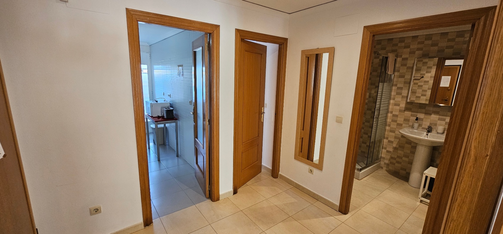 Flur mit Keramikfliesen, der die Küche, ein Schlafzimmer und ein Badezimmer mit Dusche und neutral gefliesten Wänden verbindet.