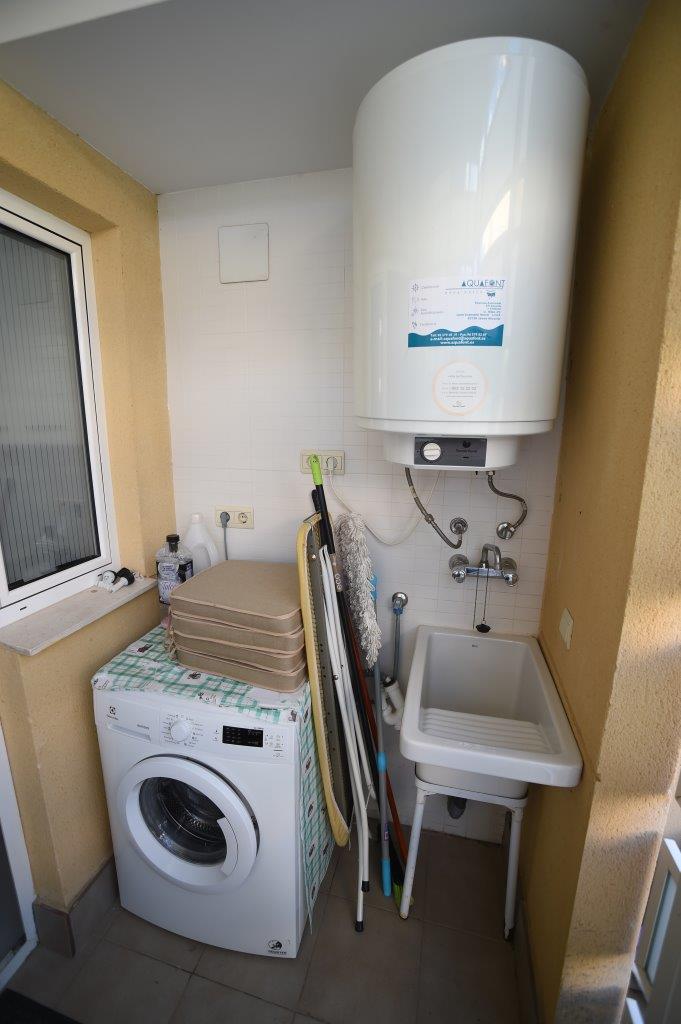 Funktionaler Hauswirtschaftsraum mit Waschmaschine, großem Elektro-Warmwasserspeicher, Ausgussbecken und Platz für Reinigungsutensilien.