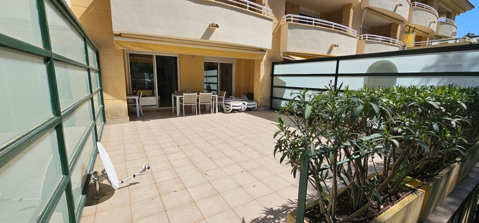 Großzügige Erdgeschoss-Terrasse mit Fliesenboden, Essbereich im Freien, Sonnenliegen und Sichtschutzwänden aus Milchglas unter einer Markise.