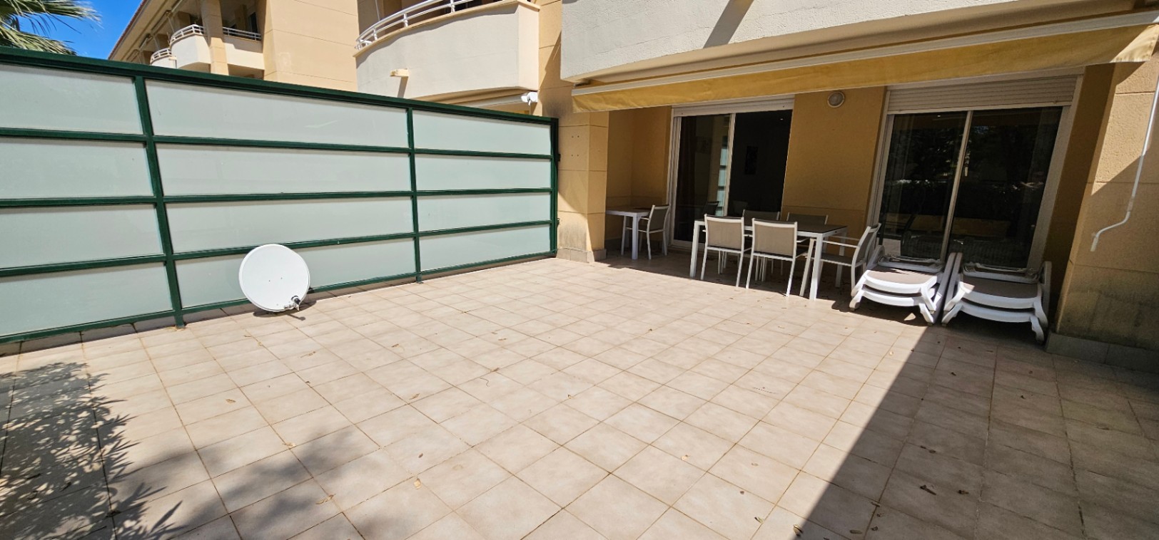Private Erdgeschoss-Terrasse mit Fliesenboden, Essbereich unter einer Markise und Sichtschutzwänden aus Milchglas.
