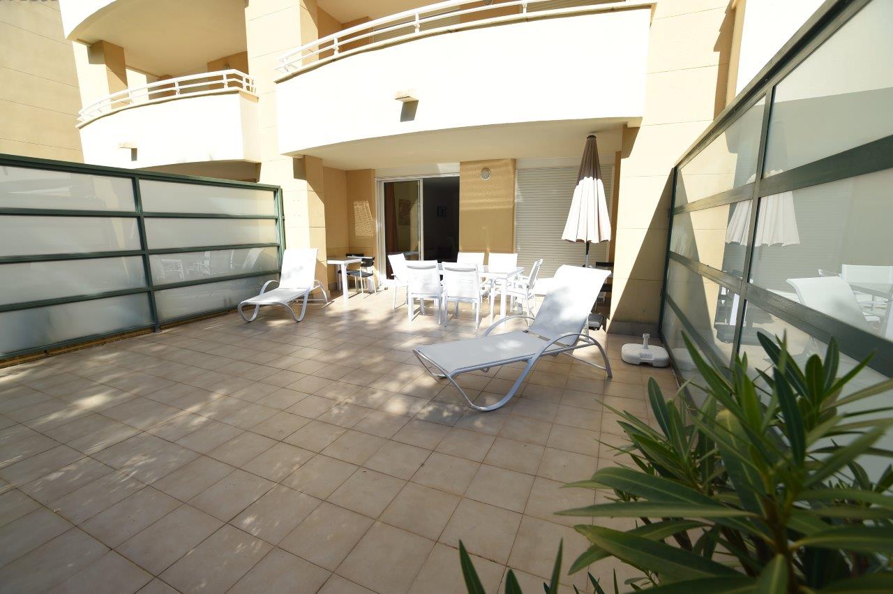 Private Erdgeschoss-Terrasse mit Fliesenboden, weißen Sonnenliegen und einem Essbereich im Freien unter der schützenden Überdachung.