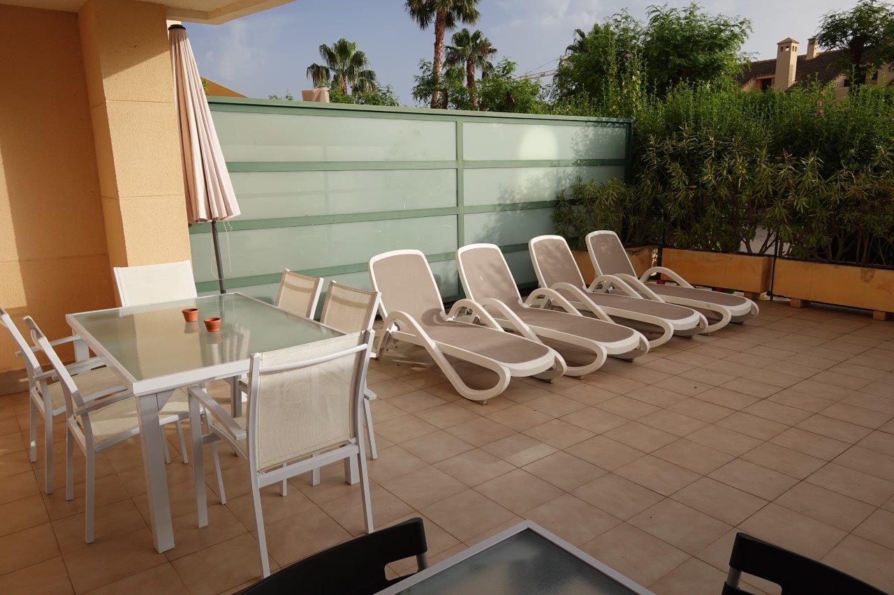 Private geflieste Terrasse mit Essbereich im Freien, Sonnenliegen und Sichtschutzwänden aus Milchglas, umgeben von mediterraner Bepflanzung.
