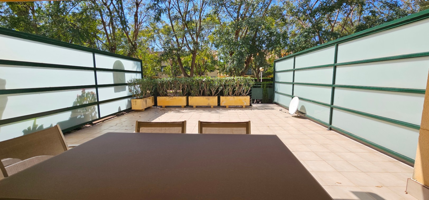 Private, geflieste Terrasse mit Sichtschutzpaneelen aus Milchglas, Pflanzkübeln und Blick auf den umliegenden Baumbestand.