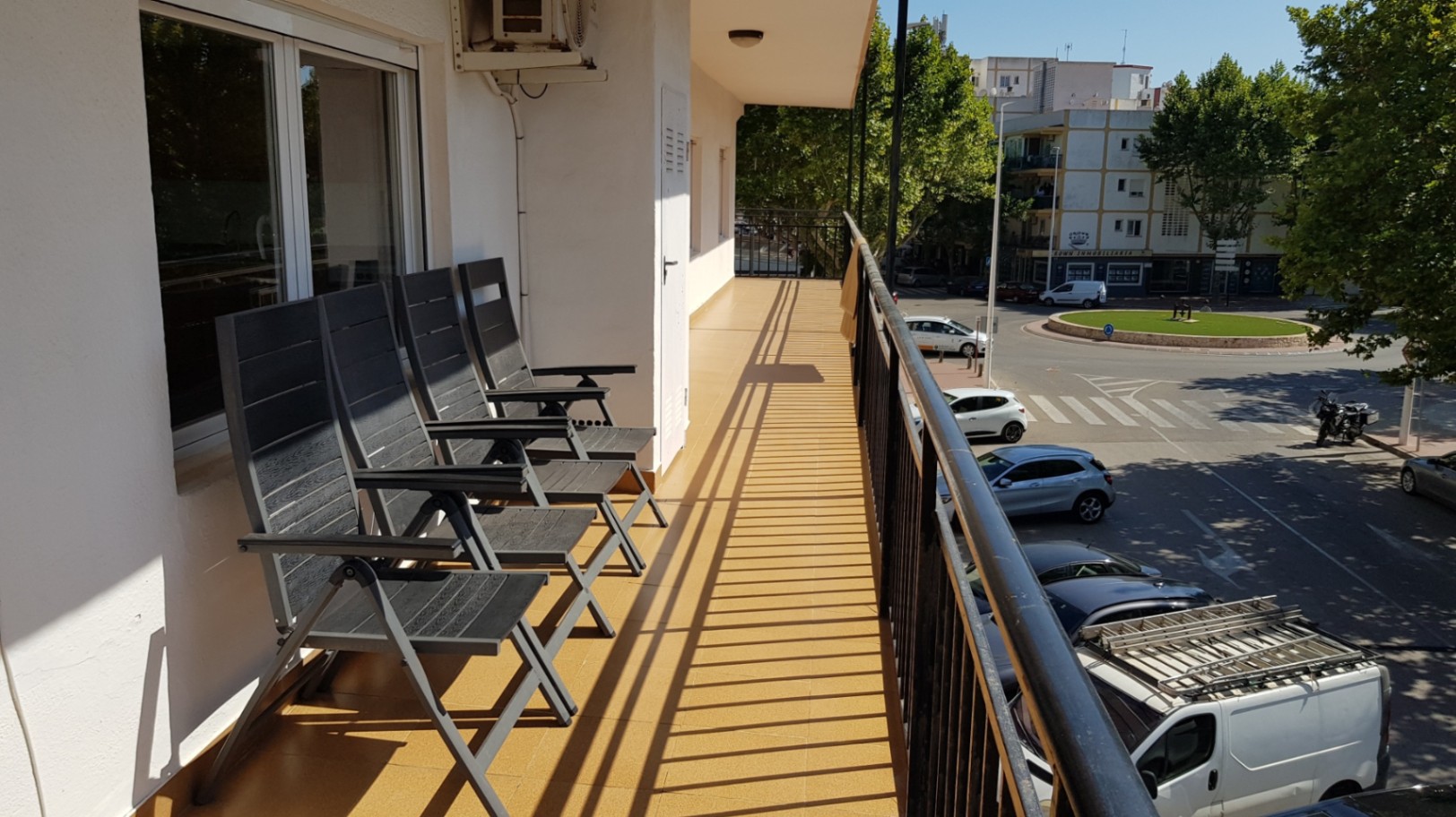 Langer Balkon mit ockerfarbenen Bodenfliesen, schwarzem Metallgeländer und Klappstühlen mit Blick auf die umliegende Stadtlandschaft von Jávea.