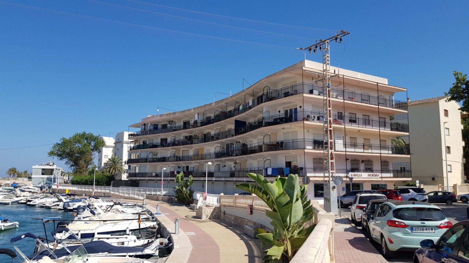 Mehrstöckiges Wohngebäude mit geschwungener Fassade direkt am Yachthafen, mit umlaufenden Balkonen und Blick auf die anliegenden Boote.