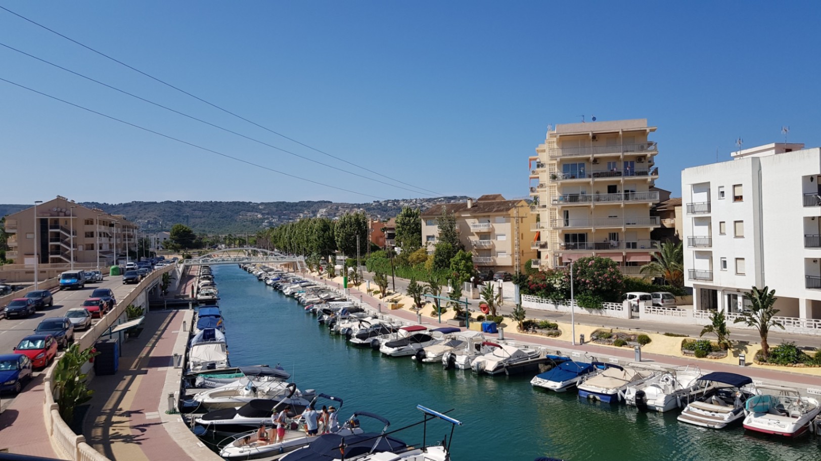 Panoramablick auf den Fontana-Kanal mit angelegten Freizeitbooten, umgeben von Wohngebäuden und der Küsteninfrastruktur von Jávea unter blauem Himmel.