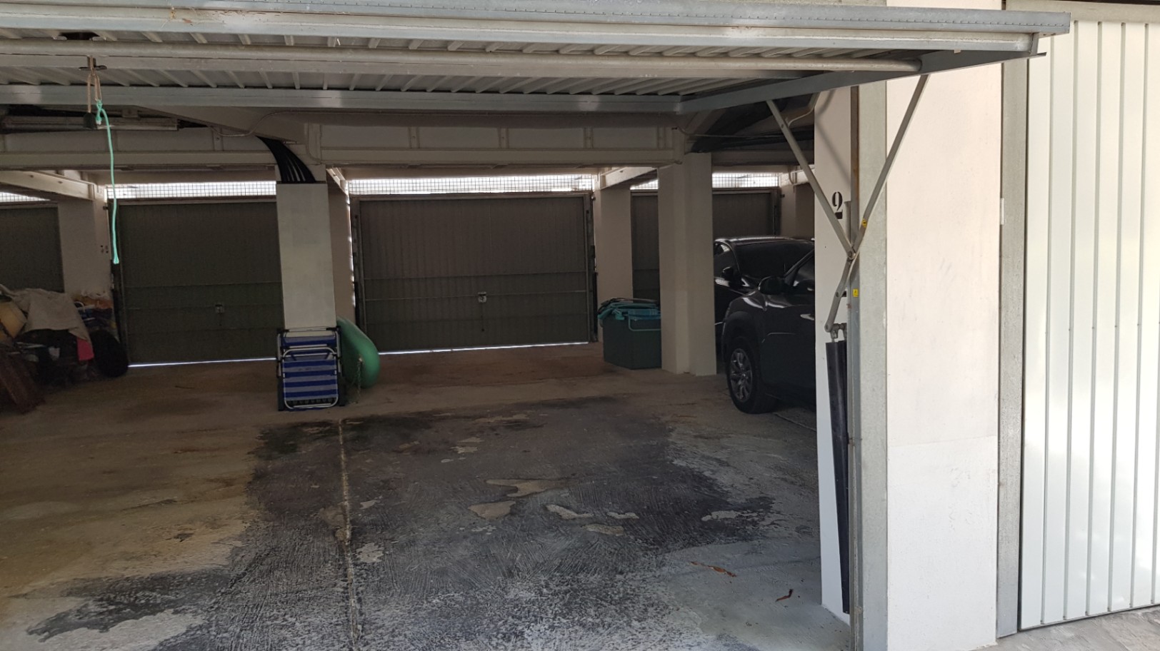 Private Tiefgarage mit Betonboden und sicheren Metall-Schwingtoren, die geschützte Parkmöglichkeiten innerhalb des Gebäudekomplexes bietet.