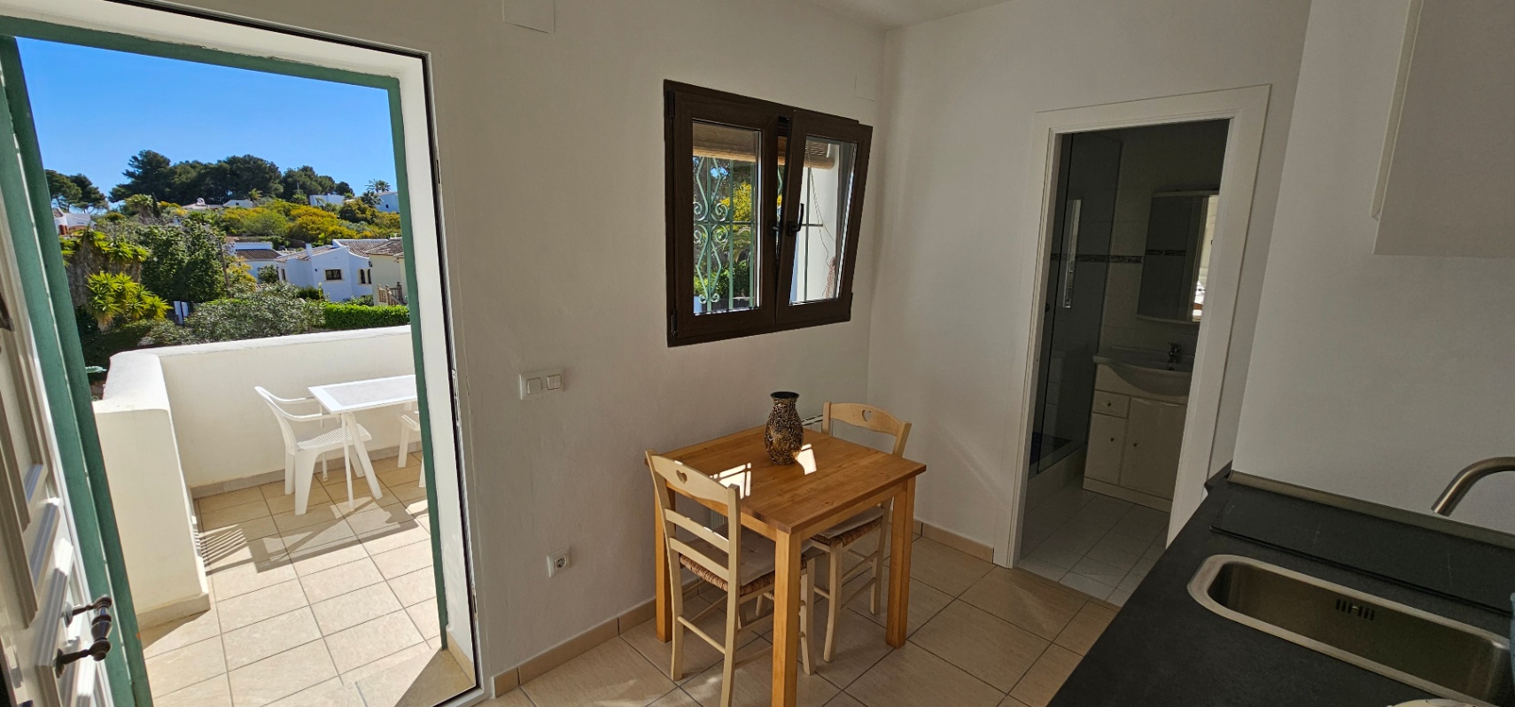 Funktionaler Essbereich mit Holztisch und Zugang zur Terrasse mit Blick auf Jávea. Der Raum verbindet die Küche mit einem angrenzenden Badezimmer.