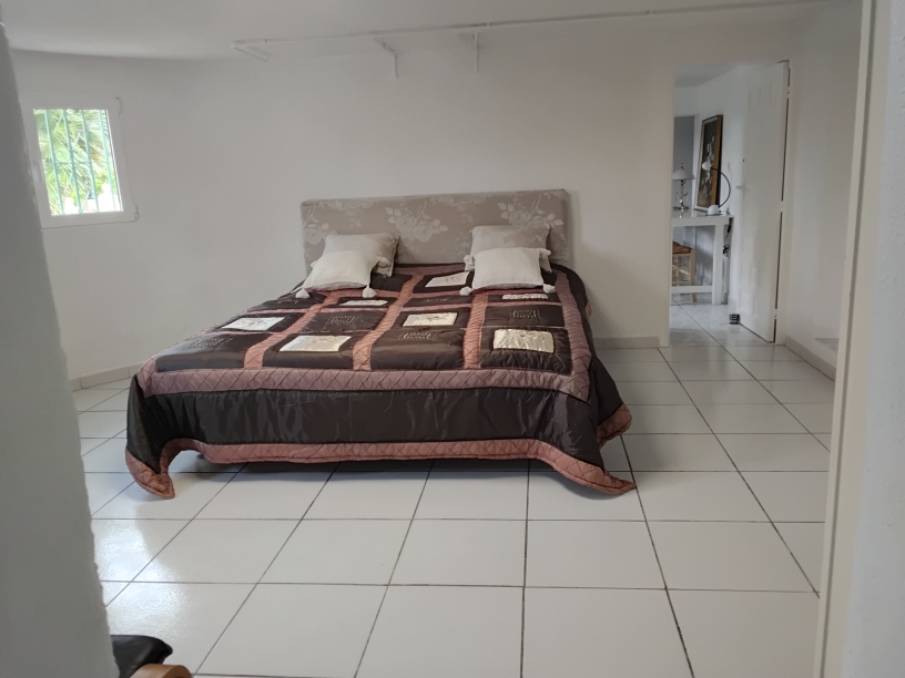 Geräumiges Schlafzimmer mit weißen Fliesenböden, Doppelbett mit floralem Kopfteil und Durchgang zu einem angrenzenden Arbeits- oder Ankleidezimmer.