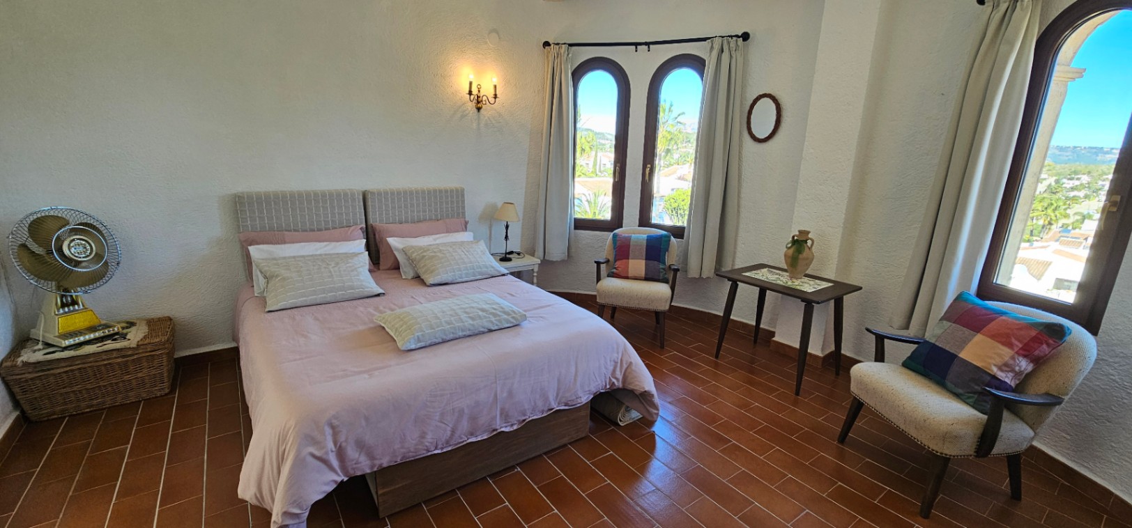 Helles Schlafzimmer mit Terrakottaboden, traditionellen Rundbogenfenstern und einer Sitzecke. Der Raum verbindet rustikalen Charme mit natürlichem Licht und Ausblick.