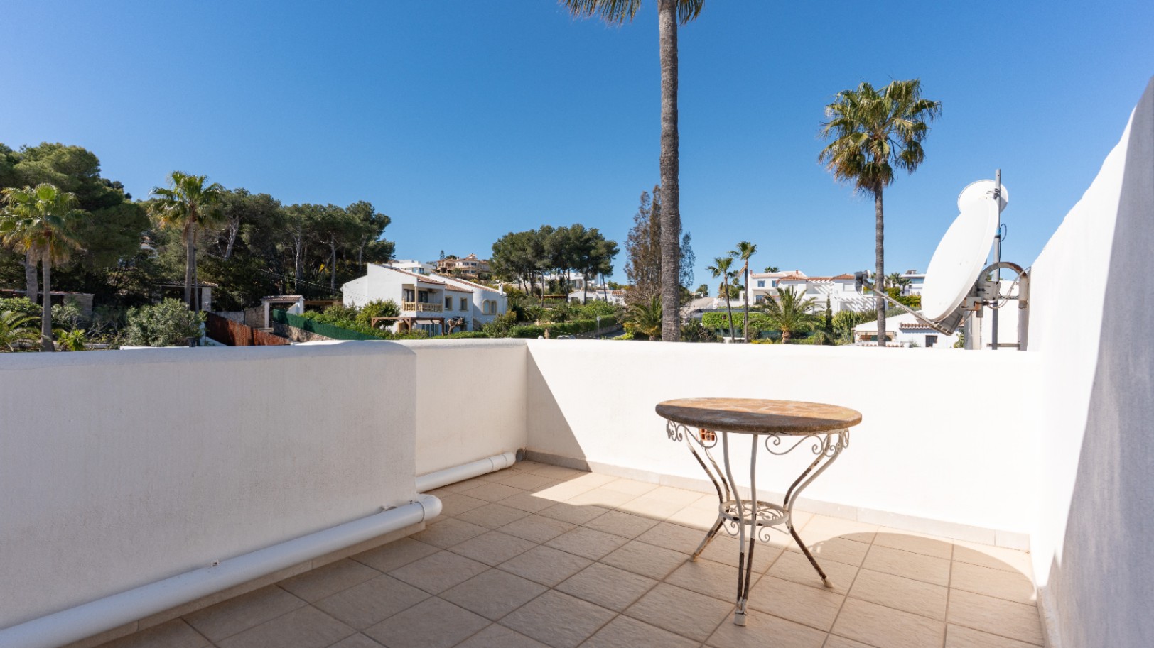 Obere Terrasse mit Fliesenboden, schmiedeeisernem Beistelltisch und Satellitenschüssel, mit weitem Blick über die umliegenden Villen und Pinien.