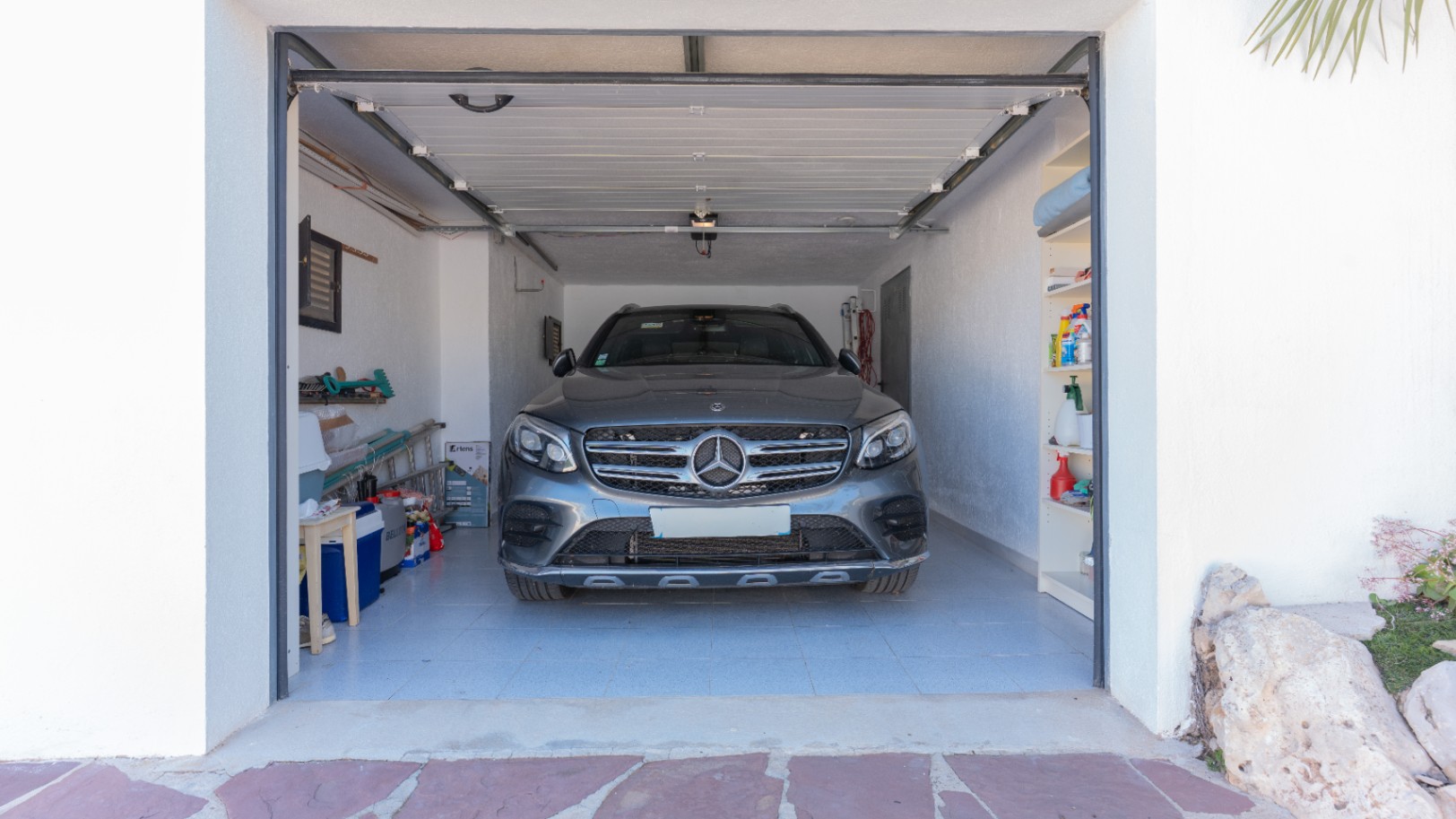 Private Garage mit Fliesenboden, integrierten Regalen und automatischem Sektionaltor, die reichlich Stauraum und sicheren Parkplatz für Fahrzeuge bietet.