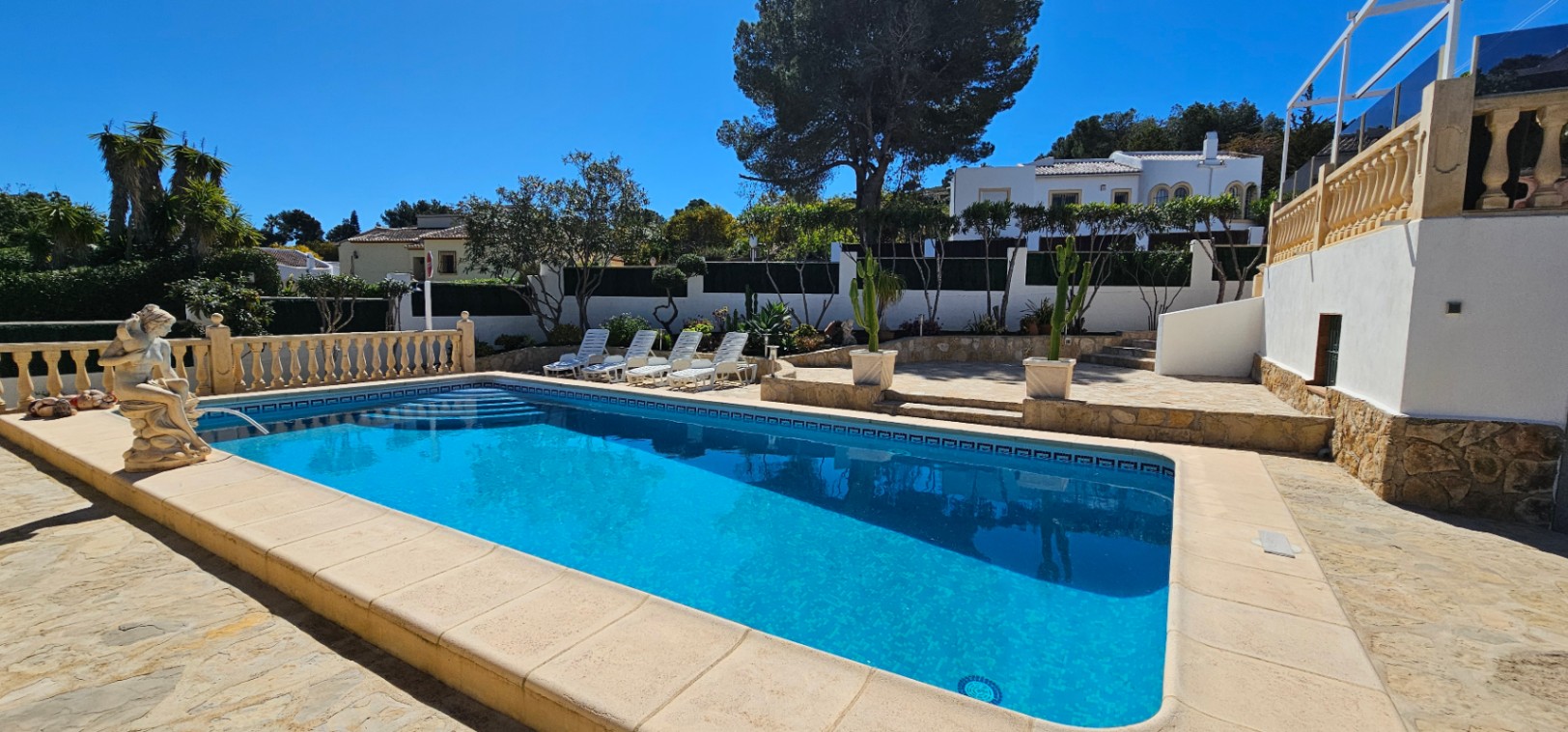 Rechteckiger Außenpool mit römischer Treppe, großzügiger Steinterrasse, Sonnenliegen und gepflegtem mediterranem Garten mit Kakteen und Pinien.