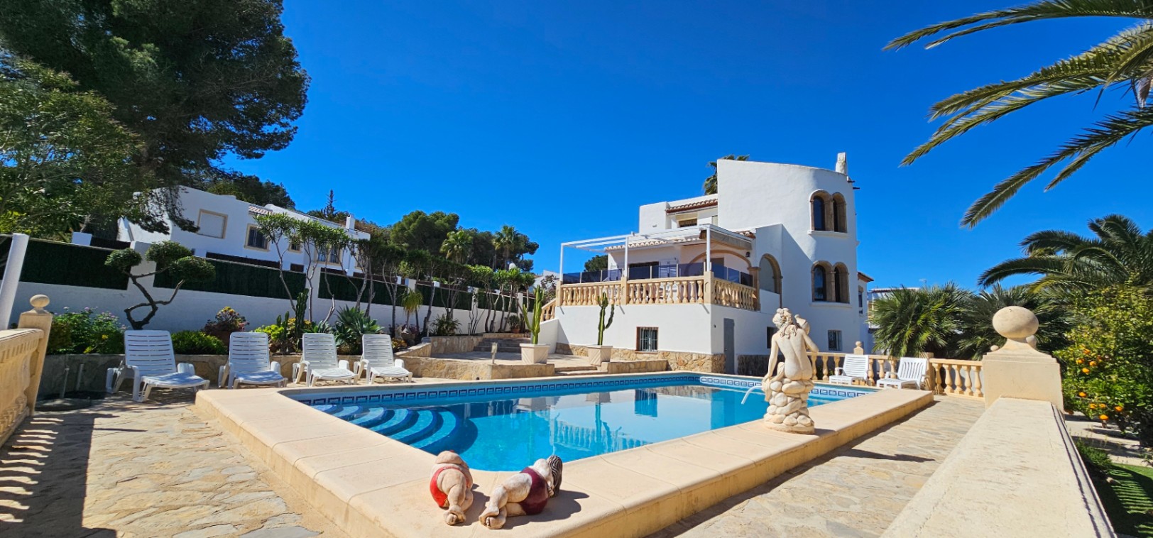 Rechteckiger Pool mit römischer Treppe, umgeben von einer Steinterrasse, weißen Liegen und einer mediterranen Villa mit markantem Rundturm.