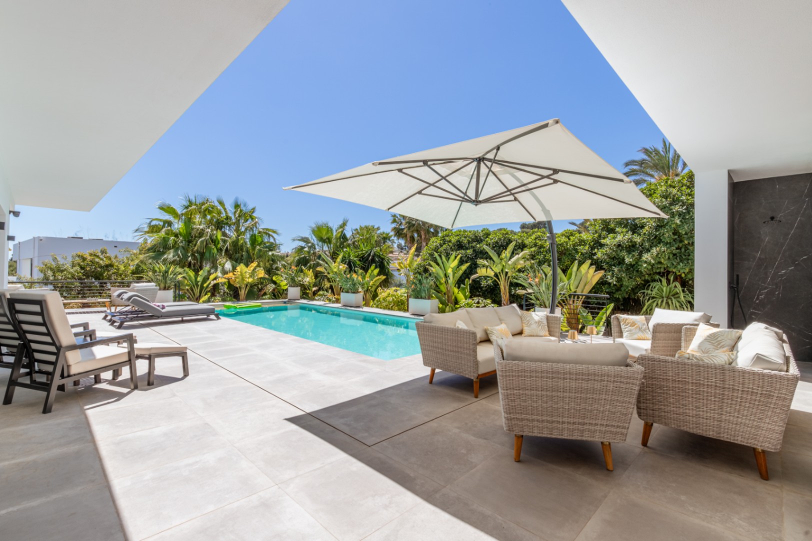 Außenbereich mit rechteckigem Pool, Lounge-Möbeln unter einem Sonnenschirm und üppiger mediterraner Bepflanzung für maximale Privatsphäre.