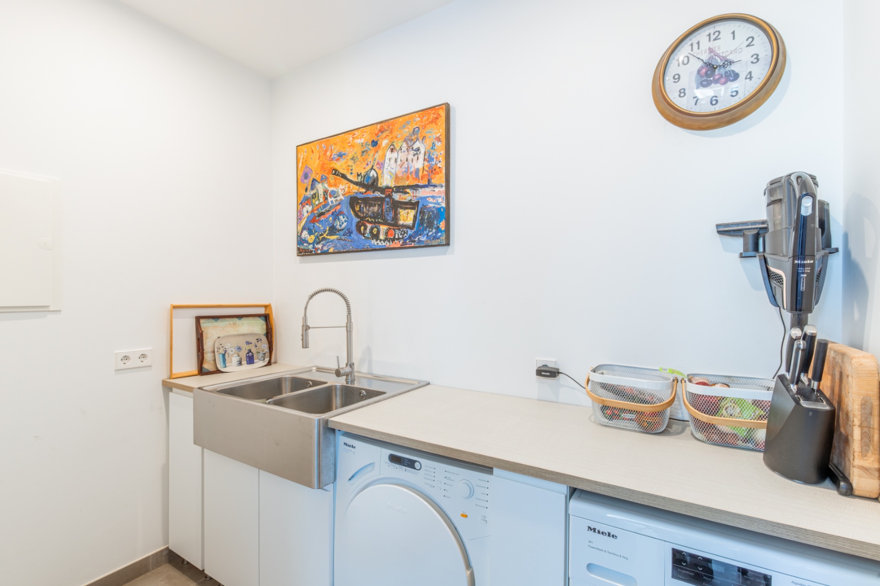 Funktionaler Hauswirtschaftsraum mit hochwertigen Miele-Geräten, einem Doppelspülbecken aus Edelstahl und einer großzügigen Arbeitsfläche in hellem Design.