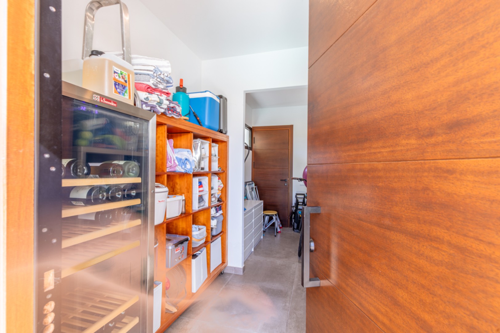 Funktionaler Hauswirtschaftsraum und Speisekammer mit Holzregalen, integriertem Weinkühlschrank und direktem Zugang durch hochwertige Holztüren.