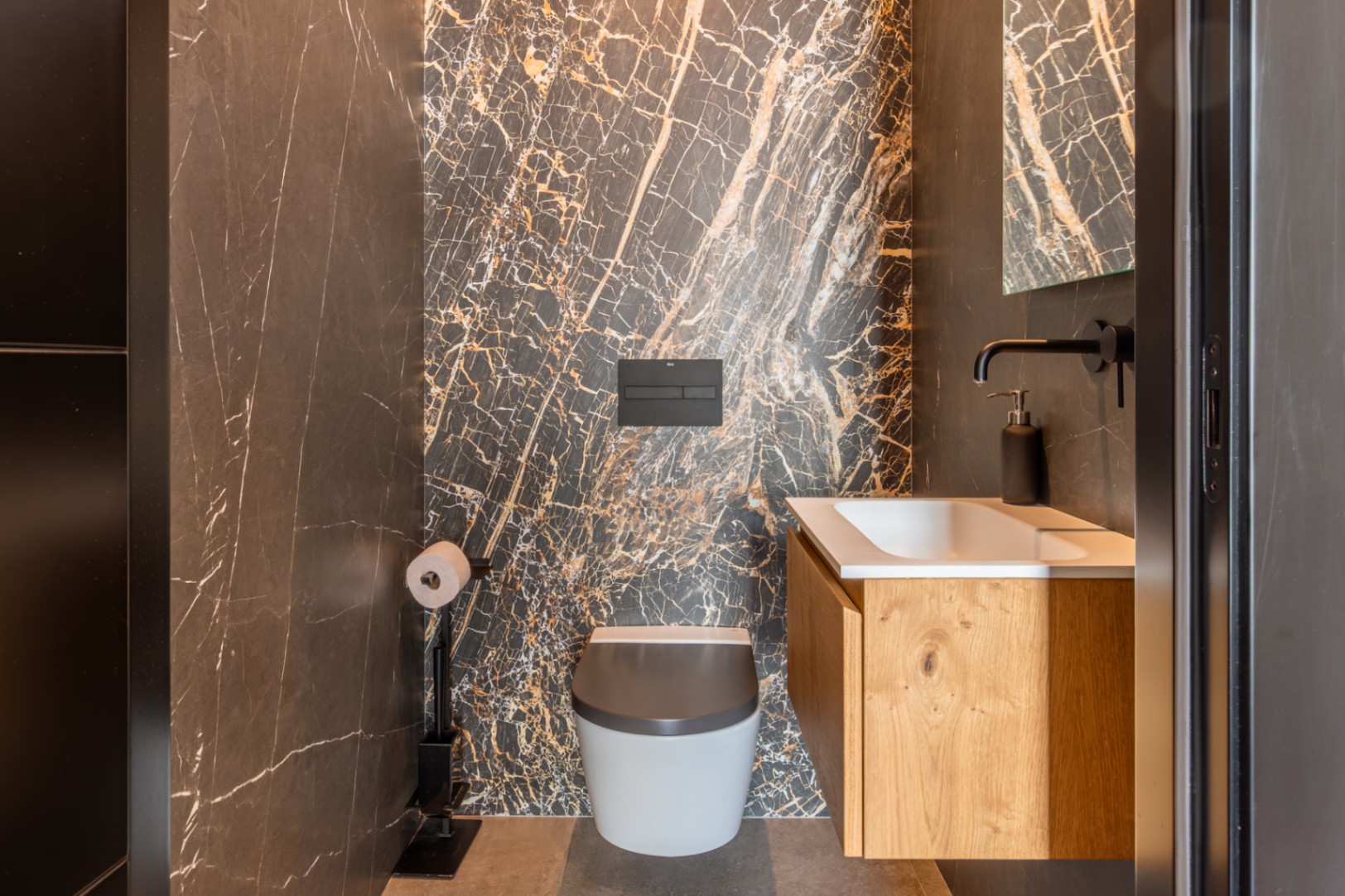 Gäste-WC mit einer Akzentwand aus dunklem Marmor mit Goldmaserung, wandhängendem WC und einem Eichen-Waschtisch mit mattschwarzen Armaturen.