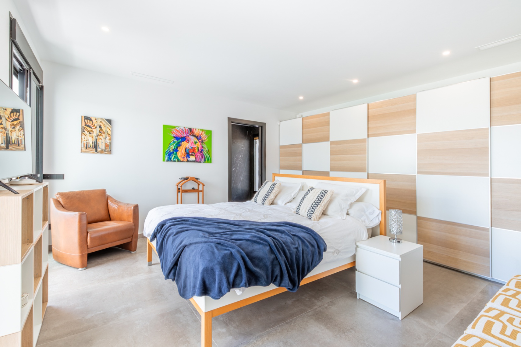 Helles Schlafzimmer mit einem wandhohen Einbauschrank im Schachbrettmuster aus Holz und Weiß, grauen Fliesenböden und einem modernen Ledersessel.