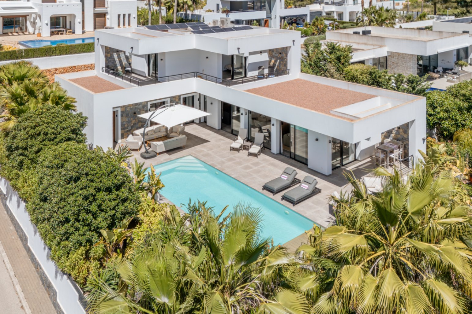Luftaufnahme der modernen Villa mit Pool, Solarmodulen auf dem Dach und großzügigen Terrassen, umgeben von privater mediterraner Vegetation.