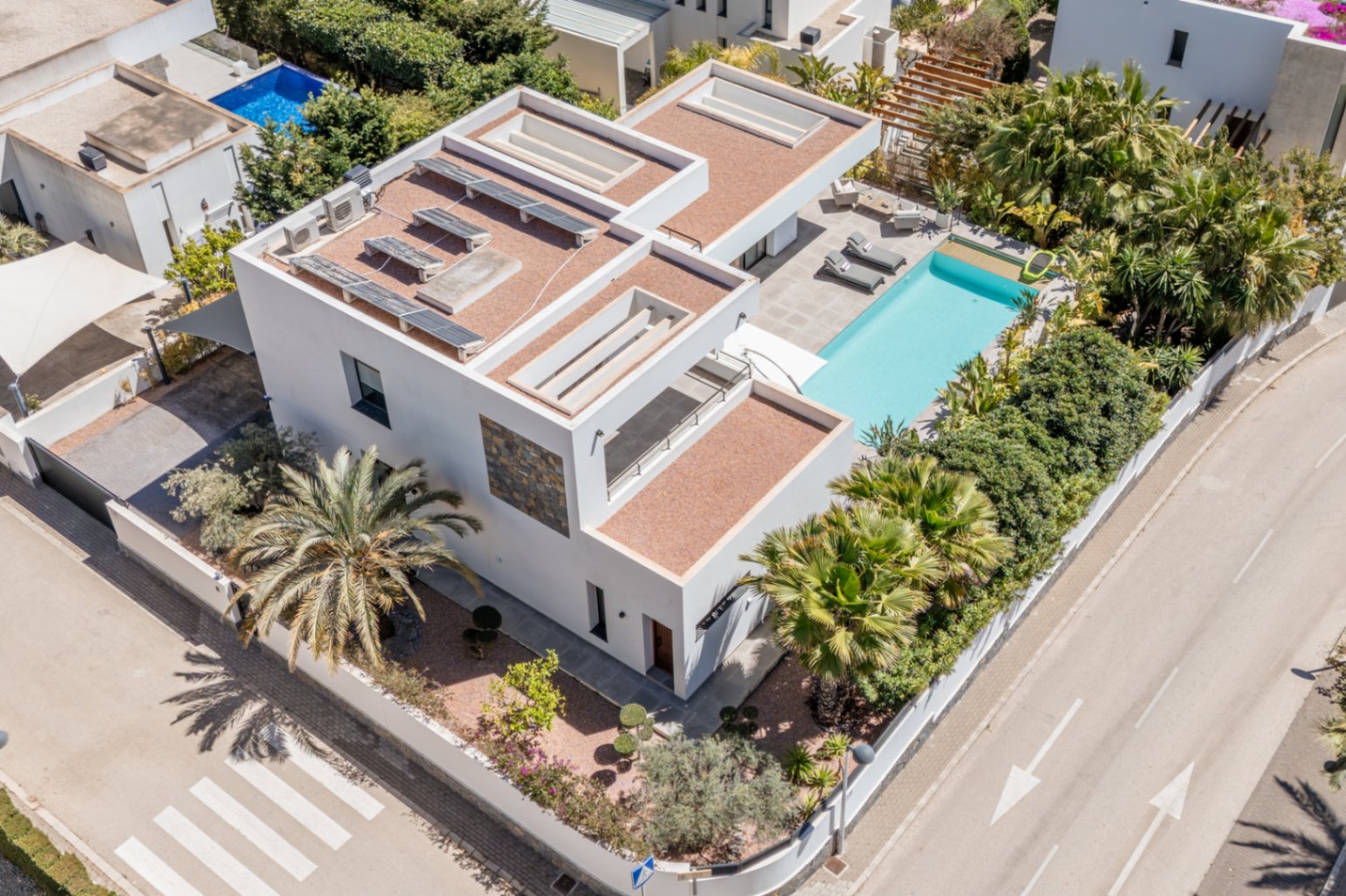 Luftaufnahme der modernen Villa mit Solarmodulen auf dem Dach, privatem Pool und mediterraner Bepflanzung, die auf dem Eckgrundstück für Privatsphäre sorgt.