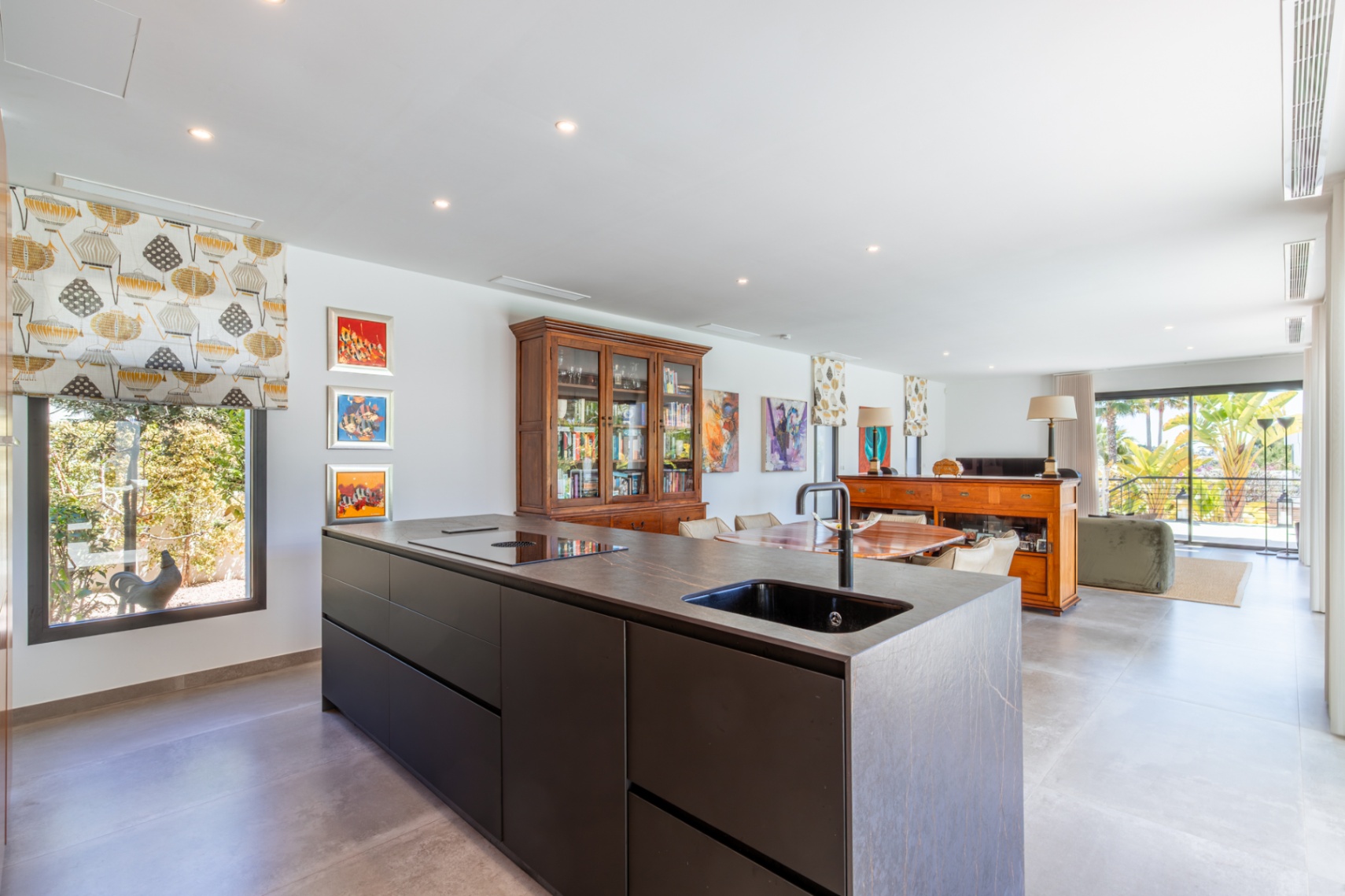 Moderne Küche mit dunkler Steininsel, integrierter Spüle und Induktionskochfeld, offen zum hellen Wohn-Essbereich mit direktem Zugang zur Terrasse.