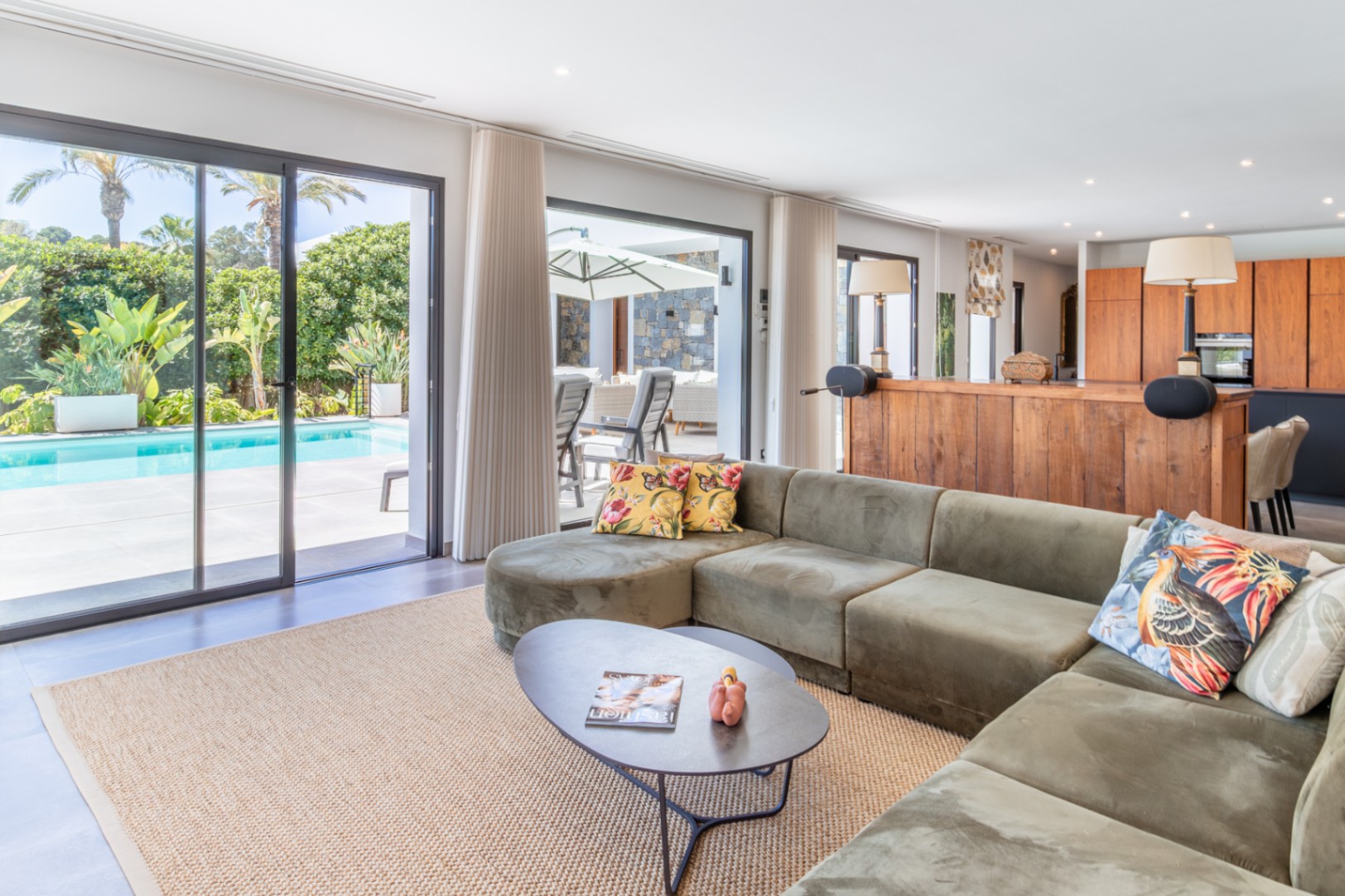 Offener Wohnbereich mit grünem Samtsofa, großen Glasschiebetüren zur Poolterrasse und integrierter Küche mit Echtholzfronten.