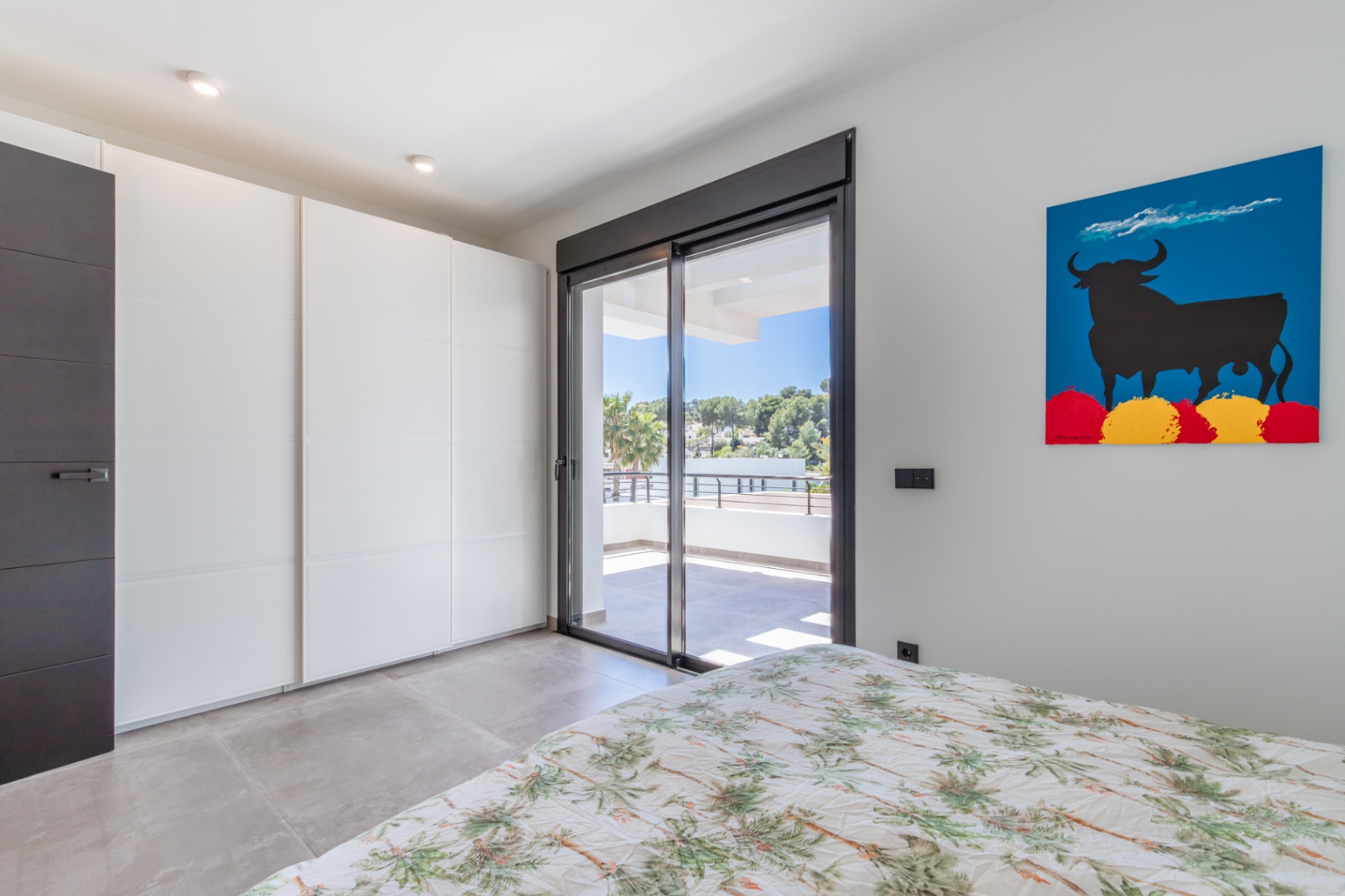 Schlafzimmer mit weißen Einbauschränken, großformatigen Fliesen und direktem Zugang zur privaten Terrasse durch bodentiefe Schiebefenster.