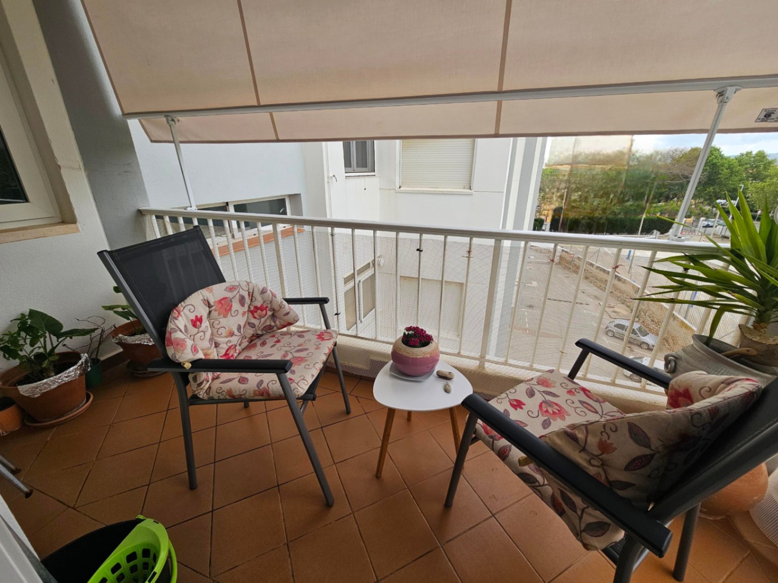 Balkon mit Terrakotta-Fliesen, ausgestattet mit einer ausziehbaren Markise und Außenmöbeln bestehend aus zwei Stühlen und einem kleinen Beistelltisch.