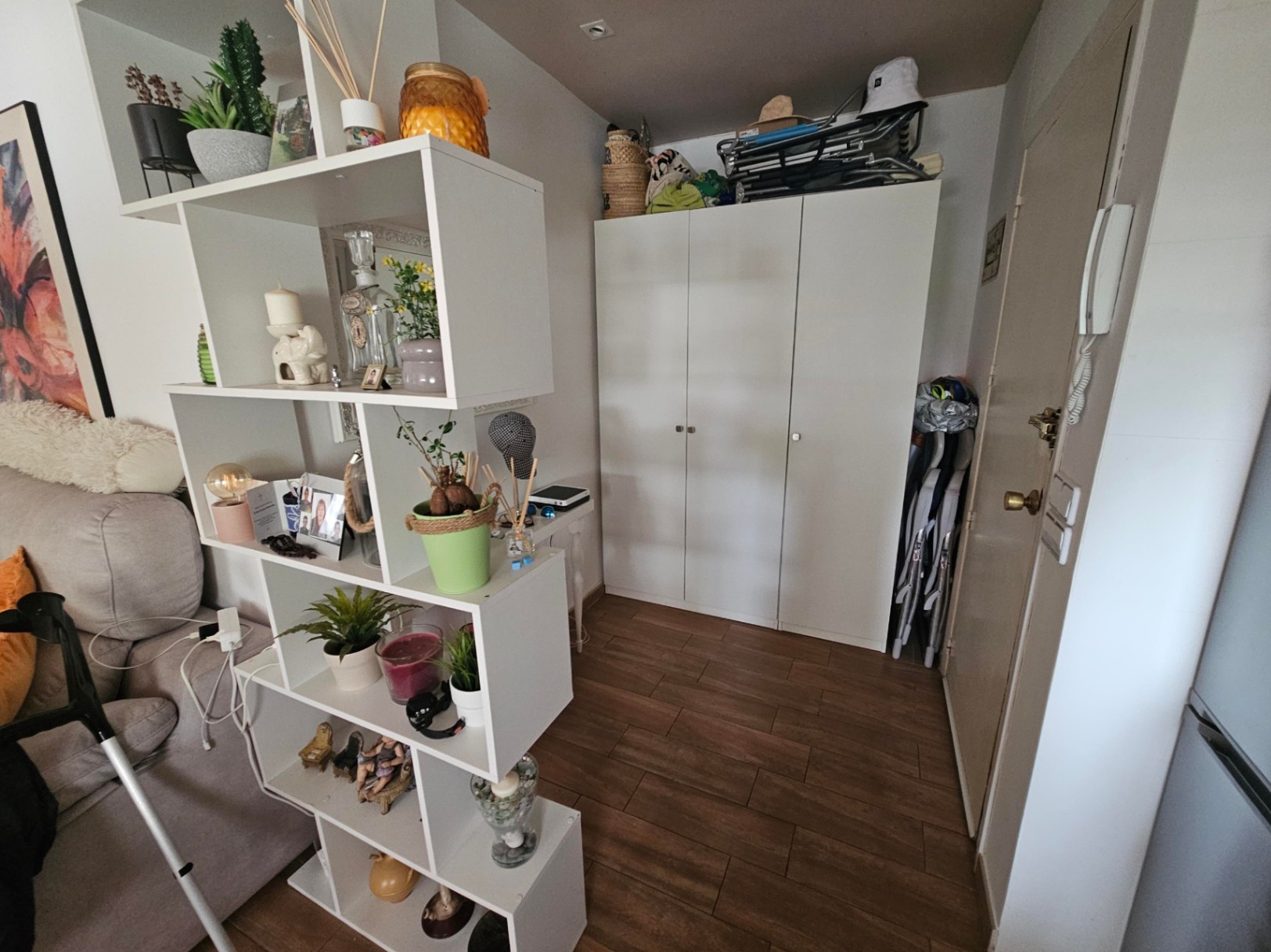 Eingangsbereich mit Fliesen in Holzoptik, einem weißen dreitürigen Kleiderschrank und einem modularen Regal als funktionaler Raumteiler.