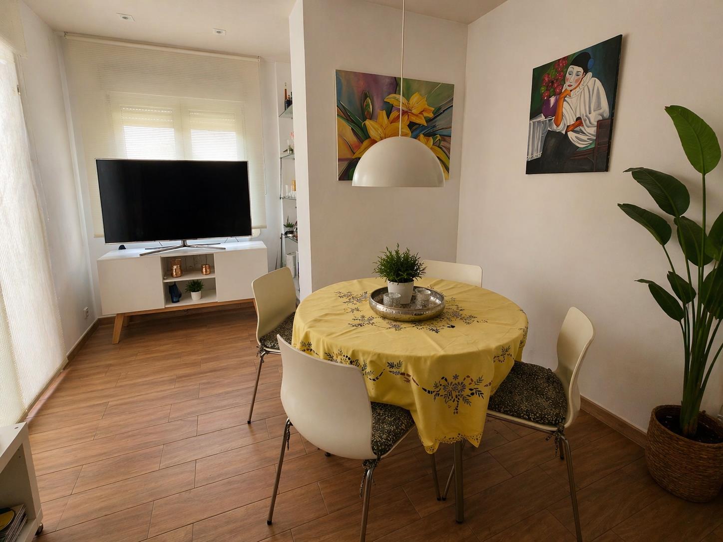 Essbereich mit rundem Tisch, weißen Stühlen und Pendelleuchte, integriert in einen hellen Wohnraum mit Bodenbelag in Holzoptik.