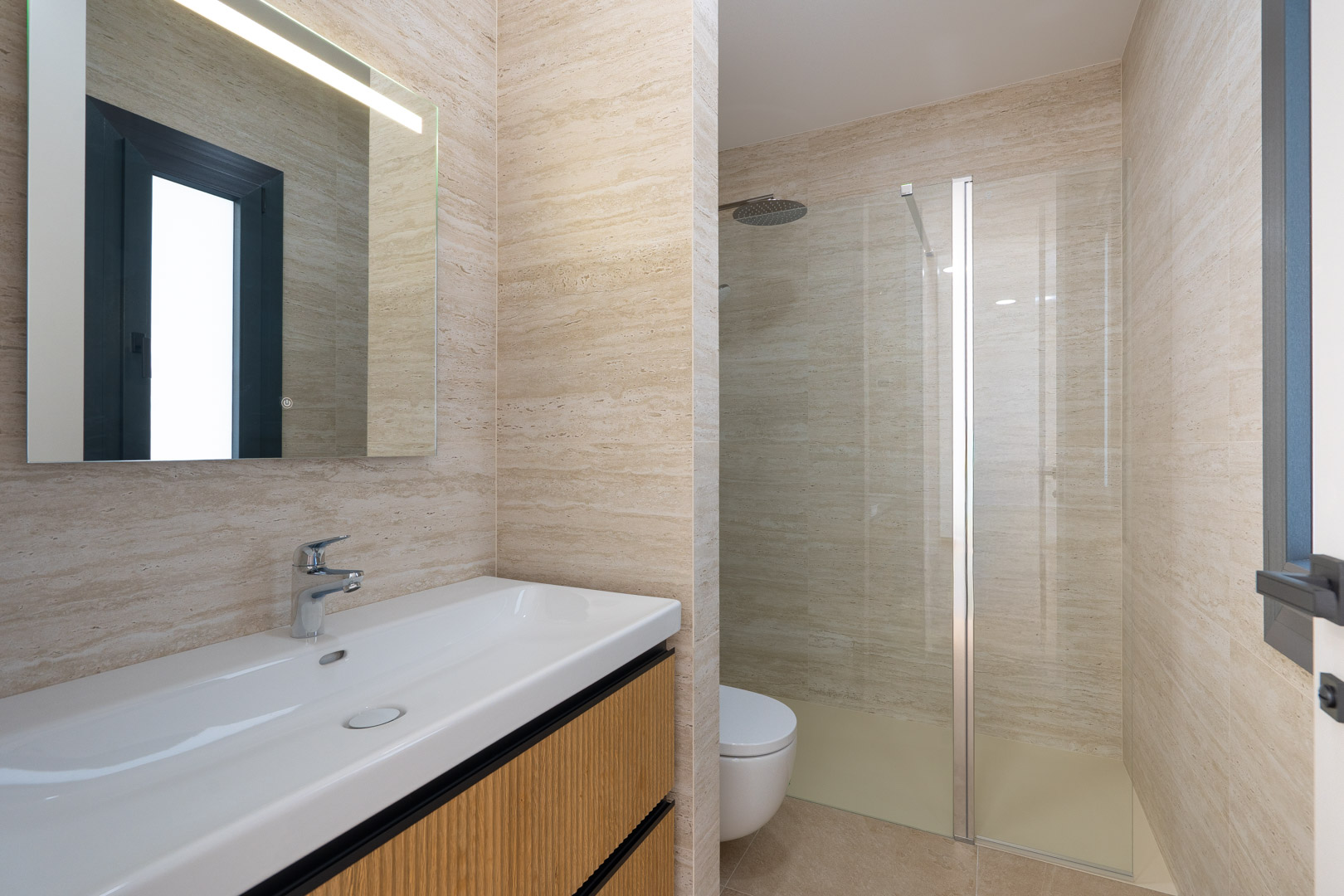 Design-Badezimmer mit Feinsteinzeug in Steinoptik, wandhängendem Waschtisch mit geriffeltem Holzdekor und begehbarer Dusche mit Glastrennwand und moderner Armatur.